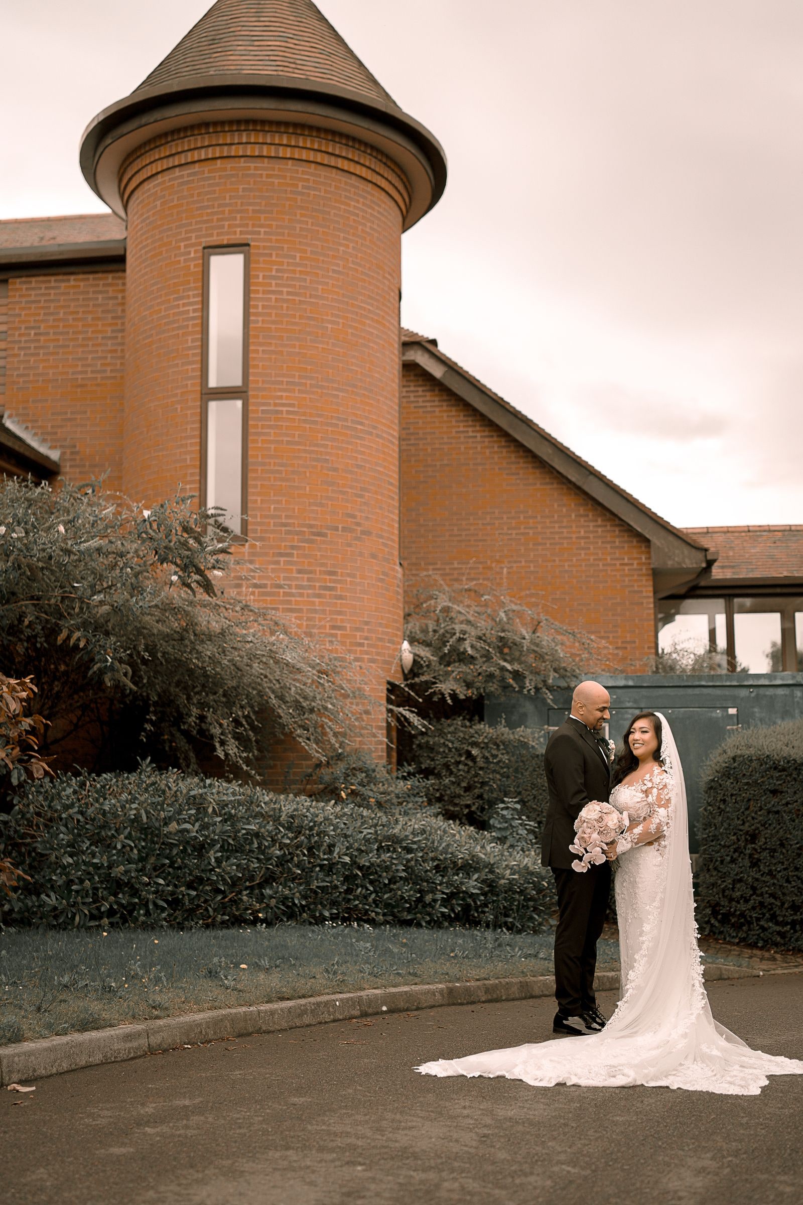Couple holding each other beside the red brick turret of the venue