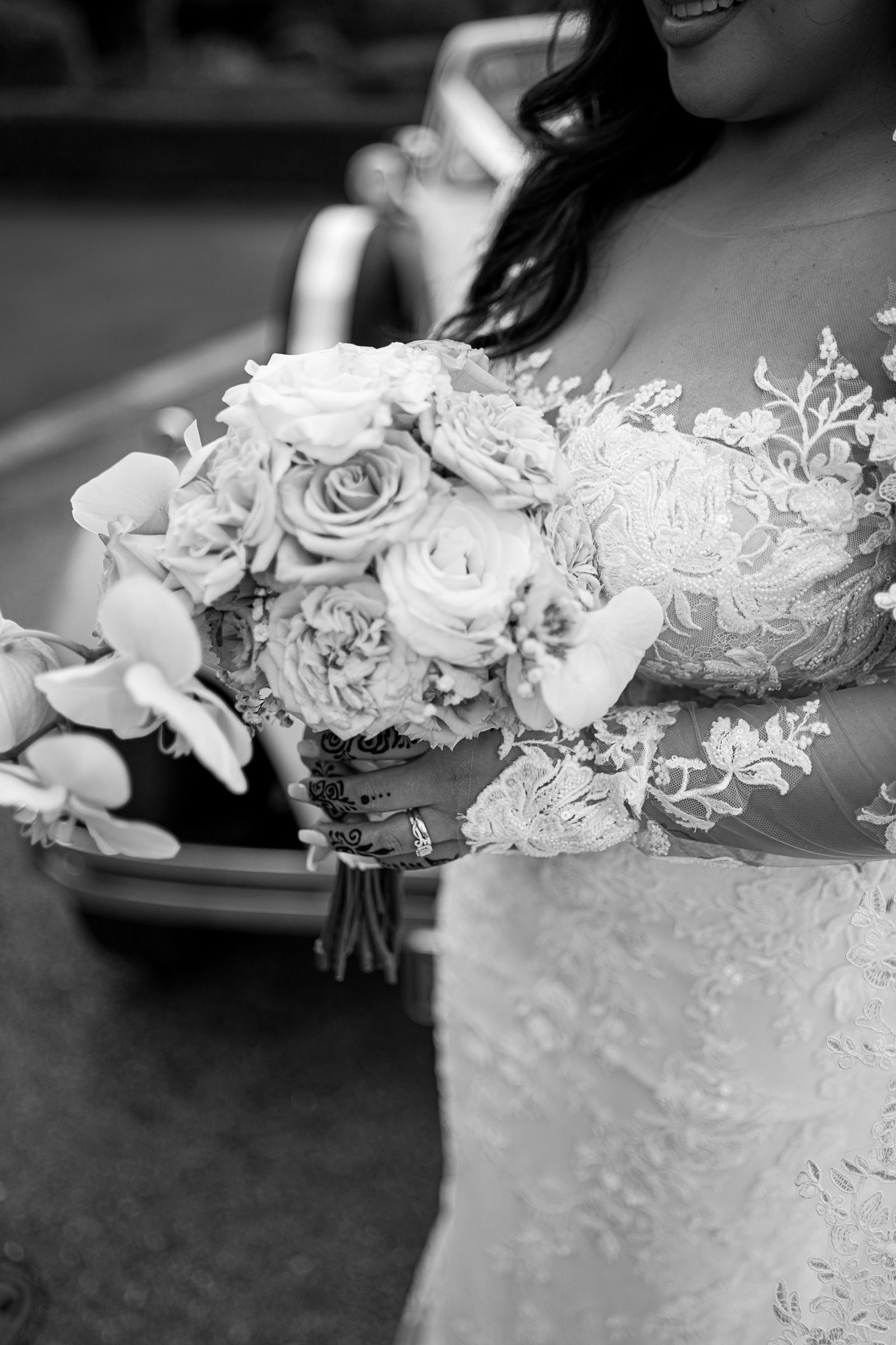 The bride's white rose bouquet held against her lace gown, in black and white
