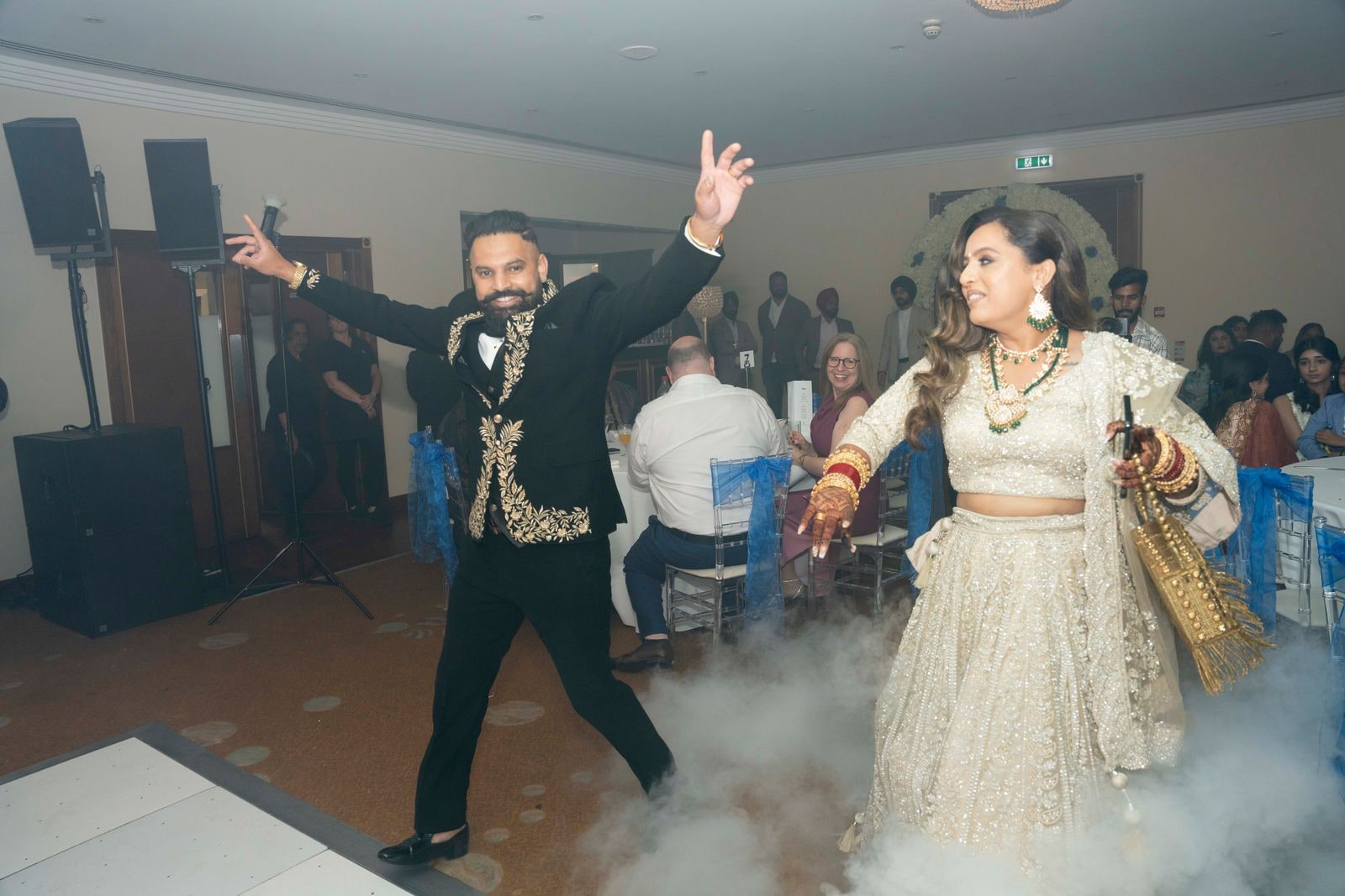 Bride and groom dancing in through dry ice at the reception, his arms flung wide