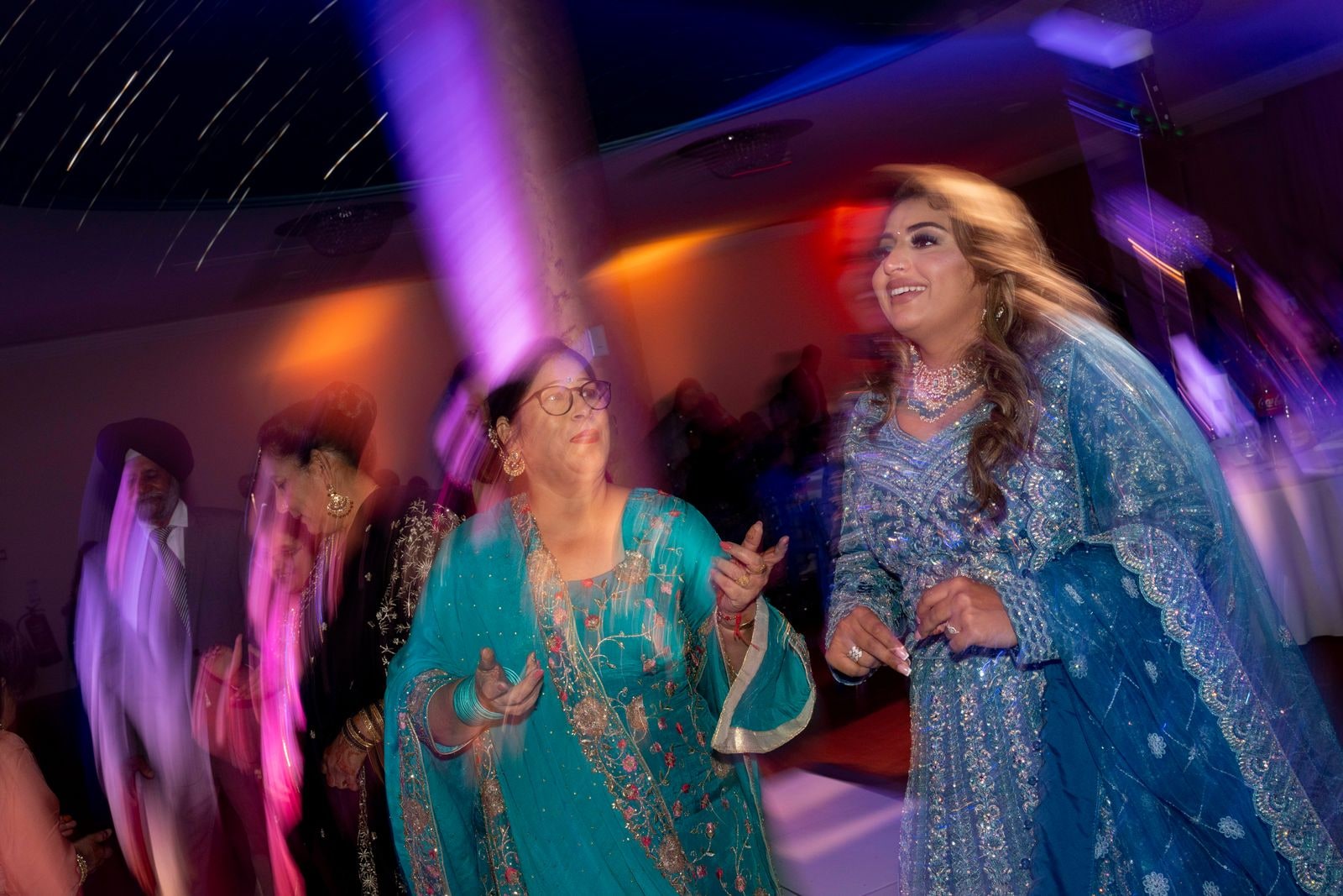 Guests dancing under coloured lights, one woman in turquoise mid step