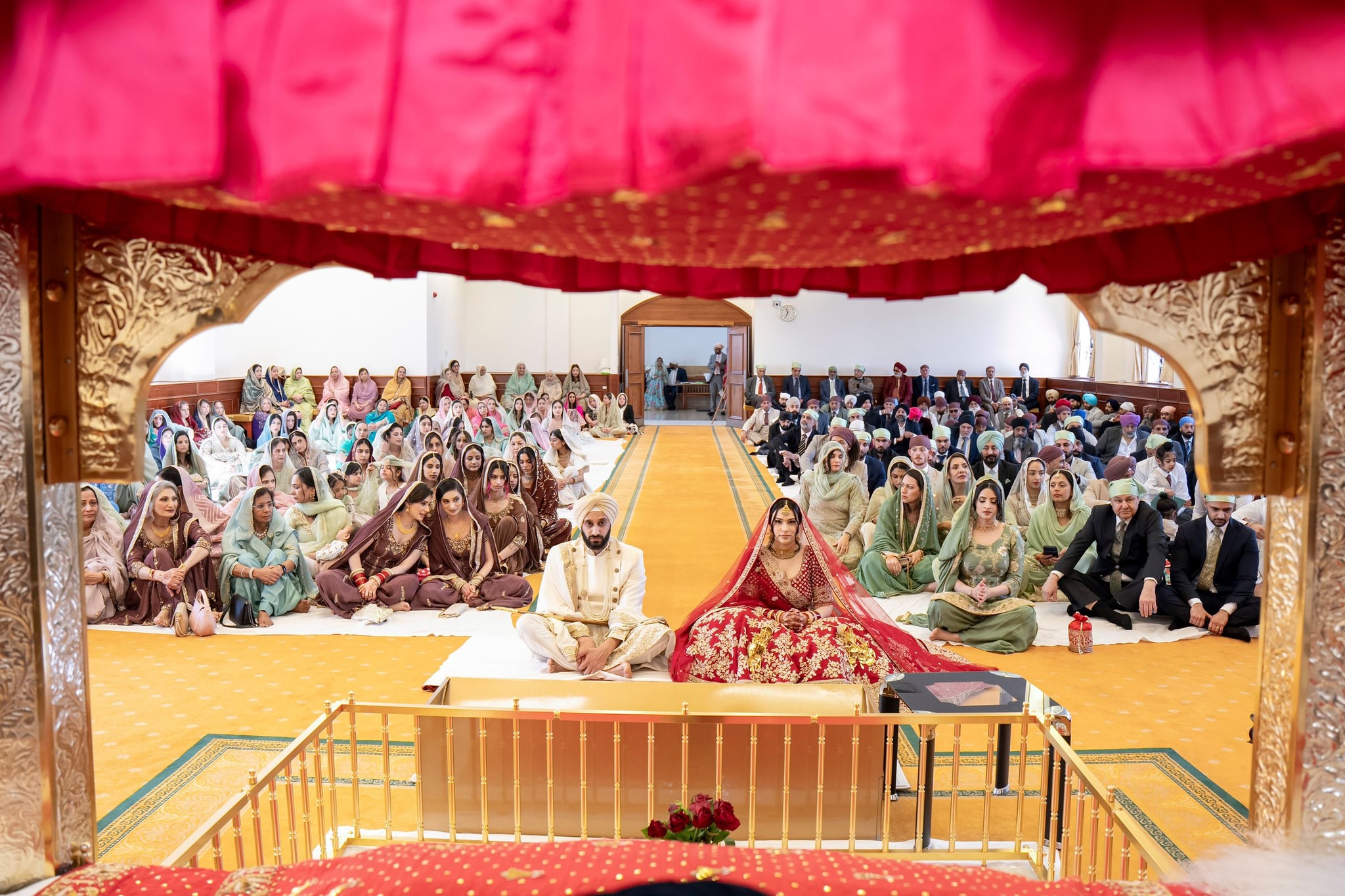 The couple seated before the congregation during the Anand Karaj, seen past the pink canopy