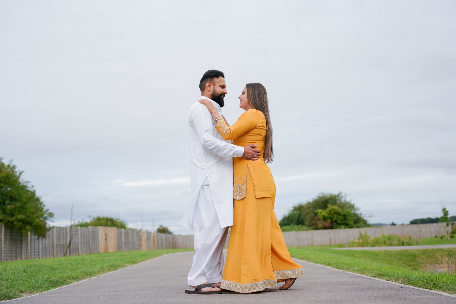 Couple holding each other on an empty suburban path, she in yellow for the haldi