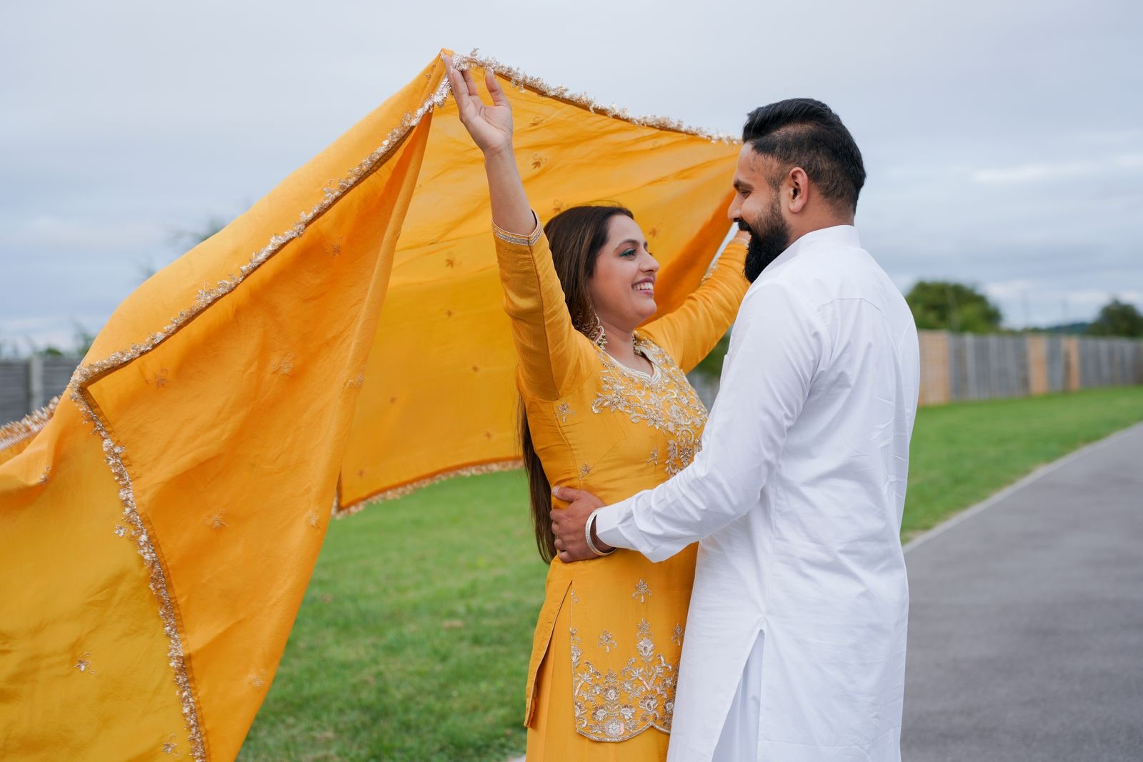 Couple holding a yellow dupatta up over themselves outdoors