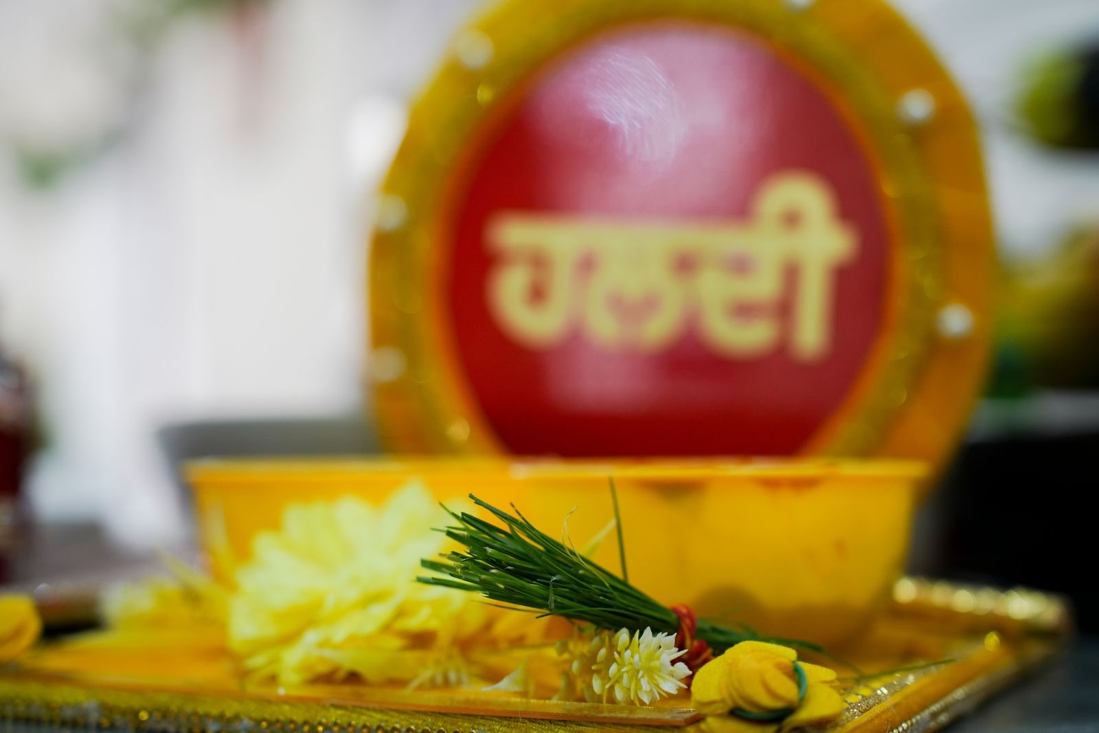A bowl labelled haldi in Punjabi set out with yellow flowers on a tray