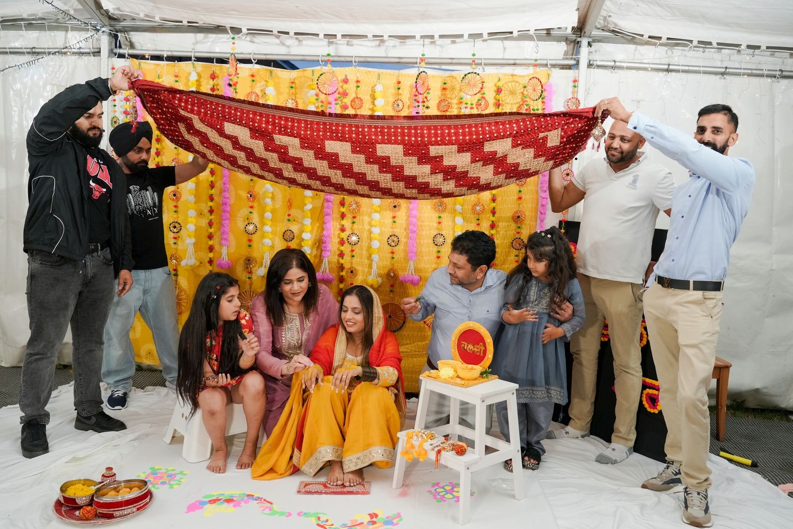 Family holding a yellow and red cloth over the bride during the haldi
