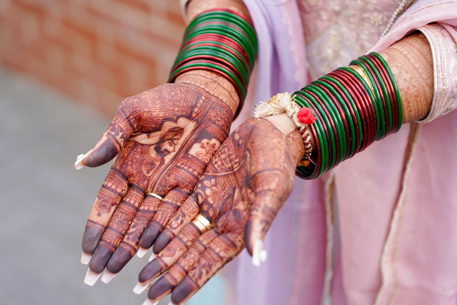 The bride's hennaed palms turned up, her wrists stacked with green and red bangles