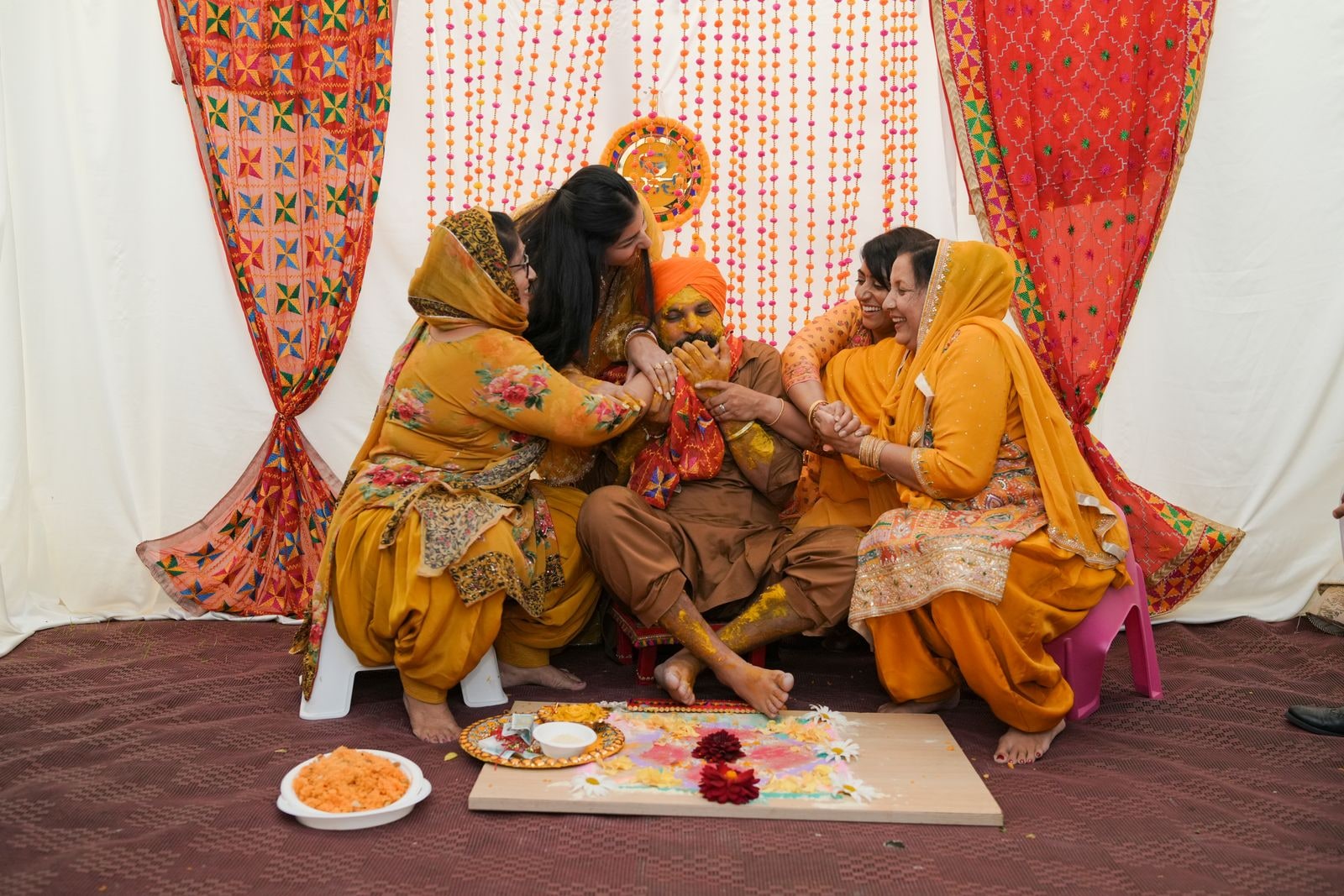 Family applying haldi paste to the couple, seated on the floor of the marquee
