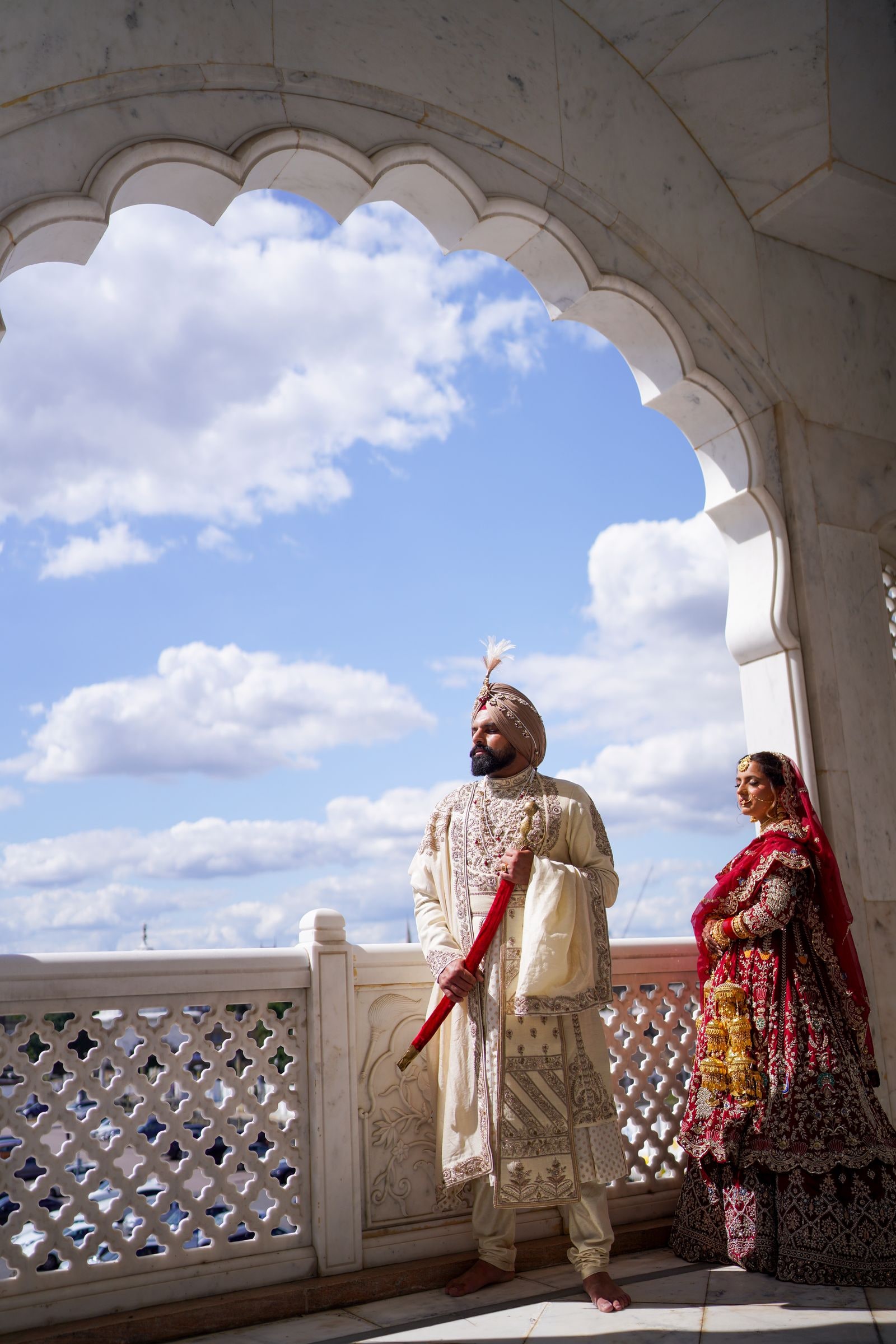 Bride and groom framed in a marble arch against a blue sky and cloud