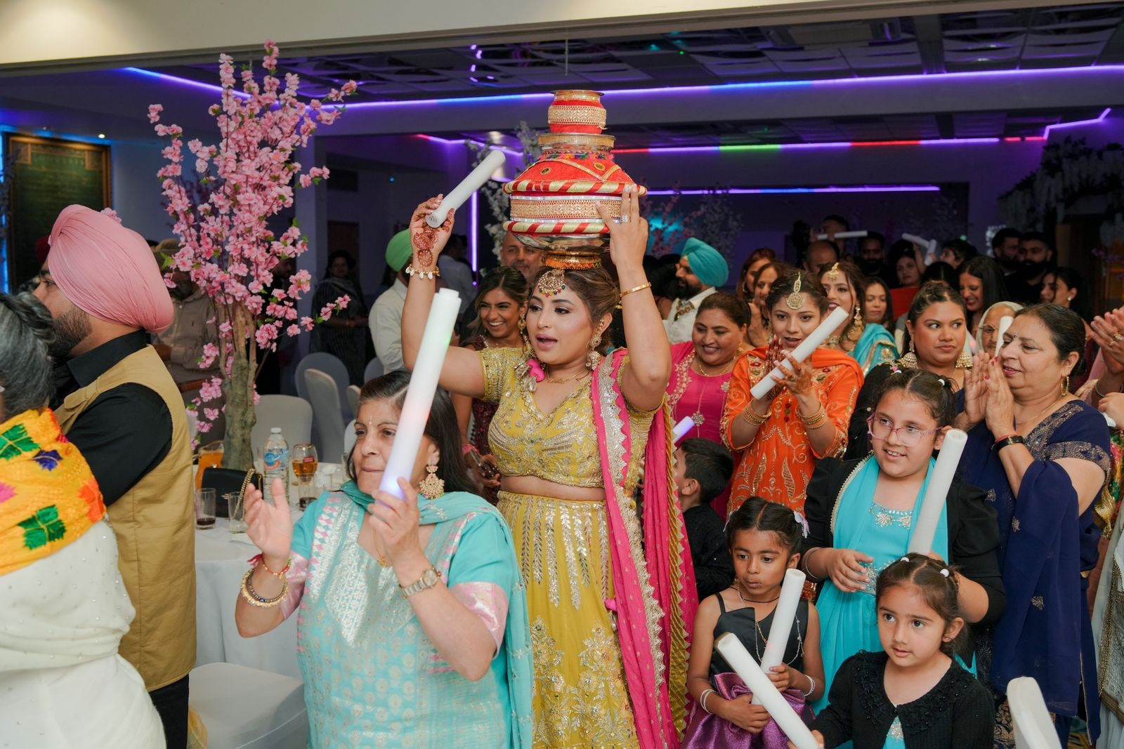 Woman carrying a decorated pot on her head into the reception, guests around her