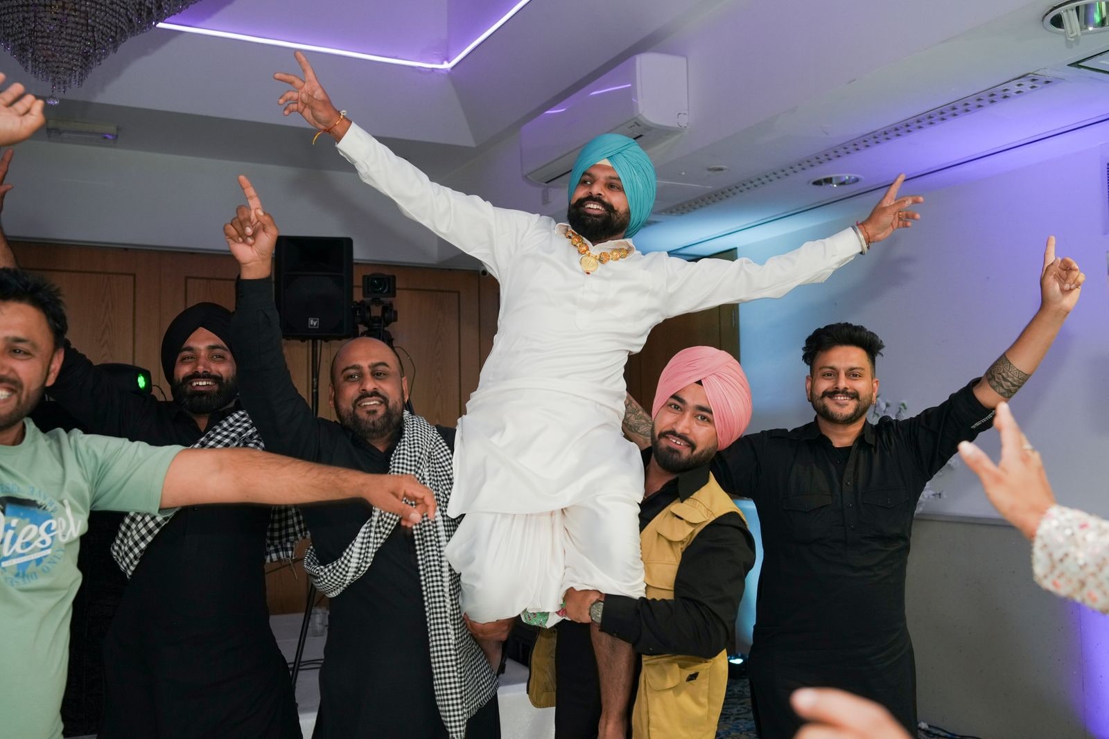 Guest in a turquoise turban lifted by his friends on the dance floor