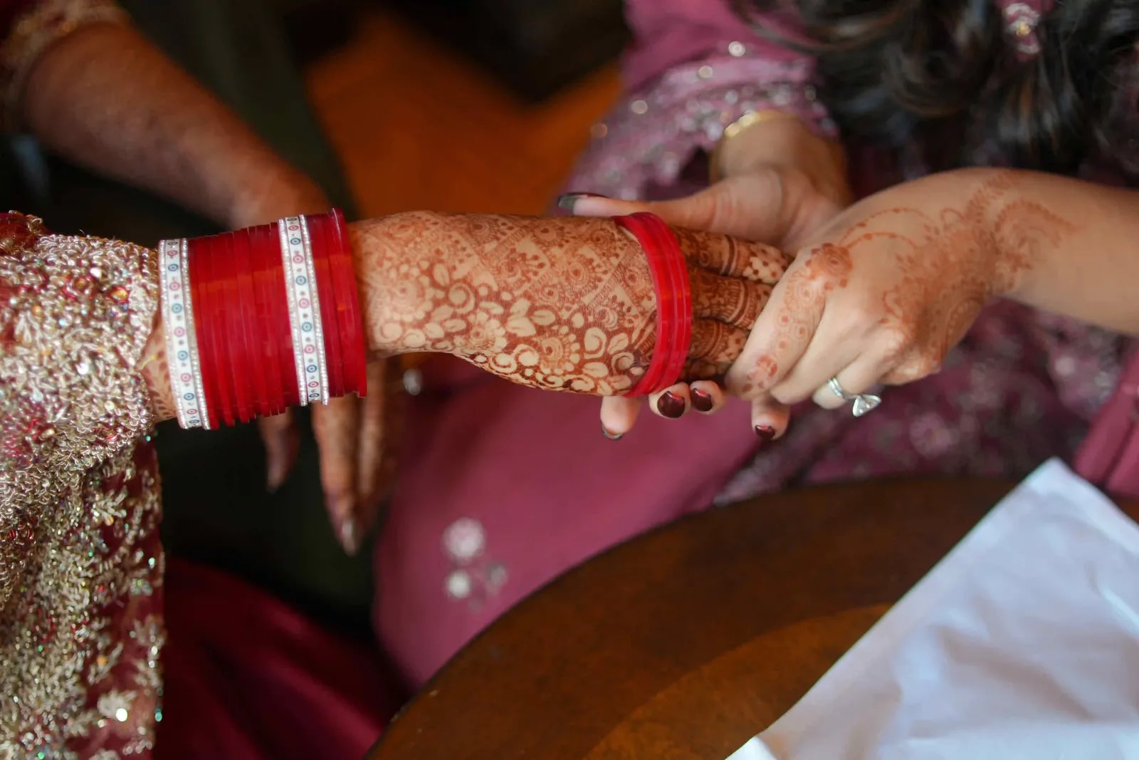 The bride's hennaed hands and red chura resting in her lap