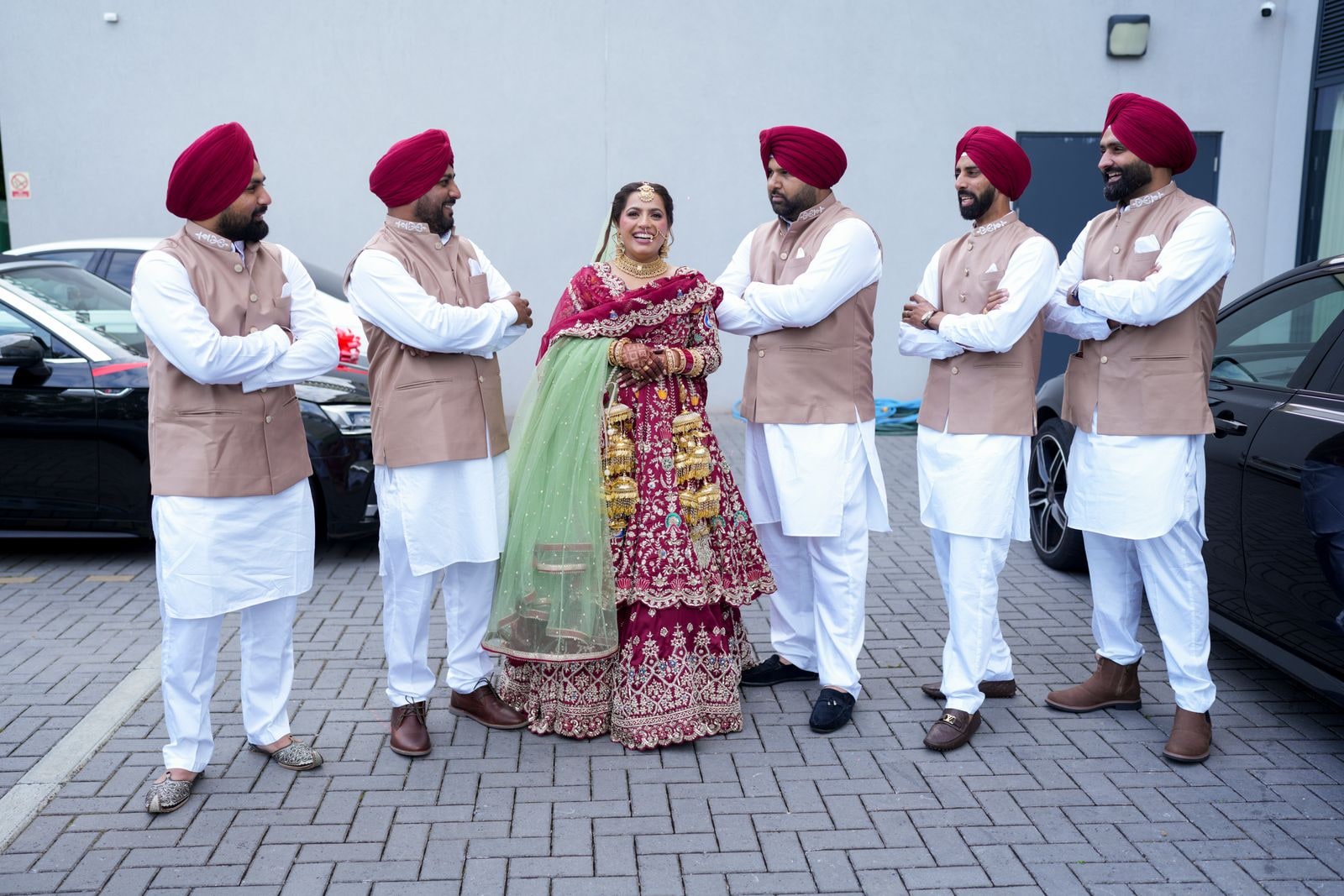 Bride in red among six men in maroon turbans and matching waistcoats