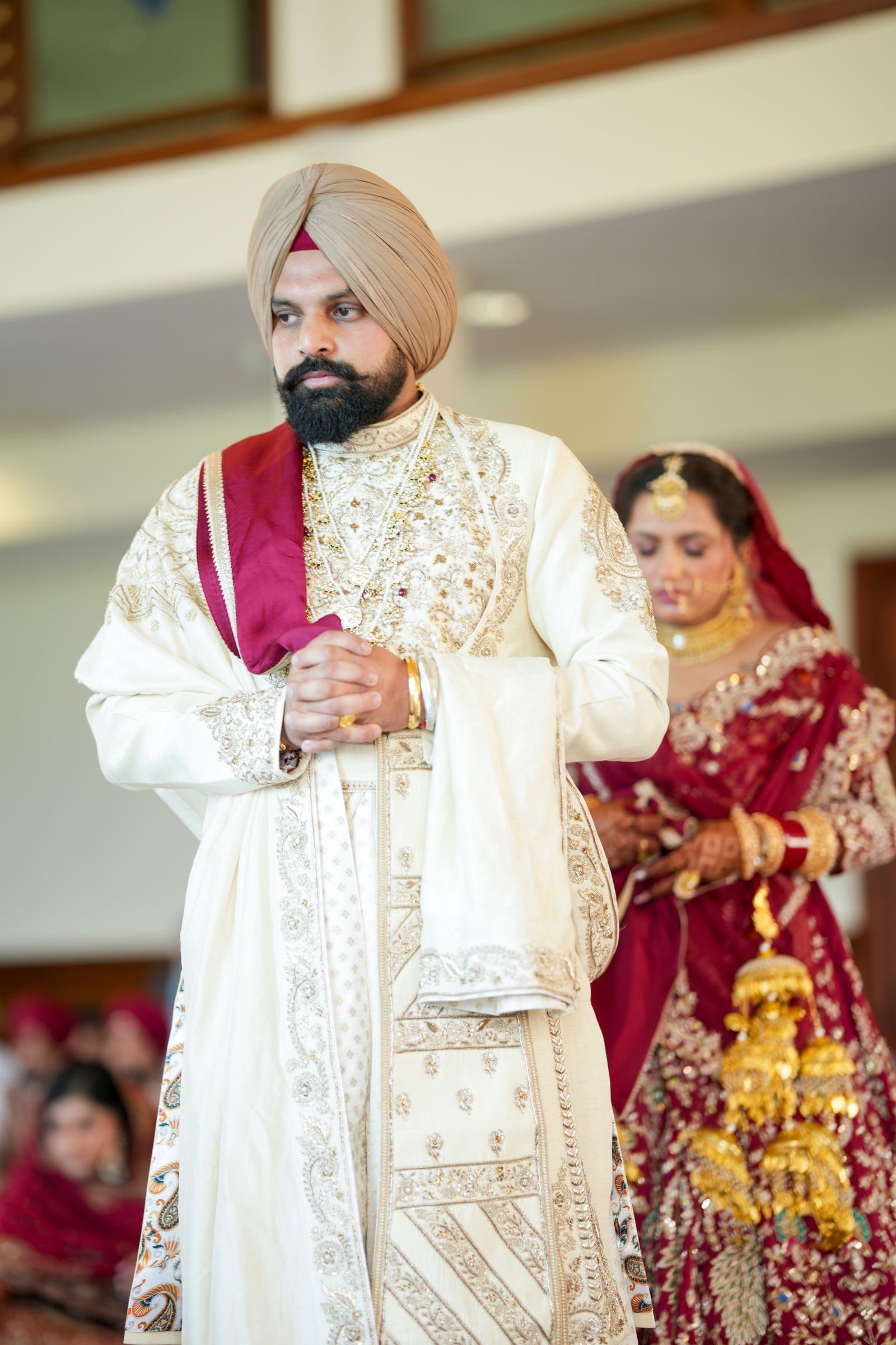 Groom in an ivory sherwani and turban with his bride close behind him