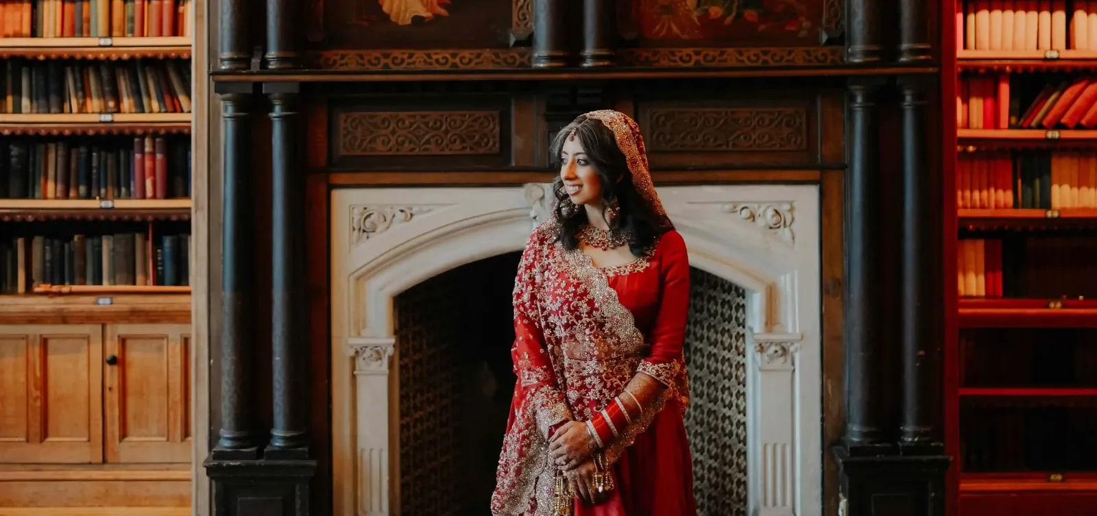 Bride standing before a carved fireplace, bookshelves rising on either side
