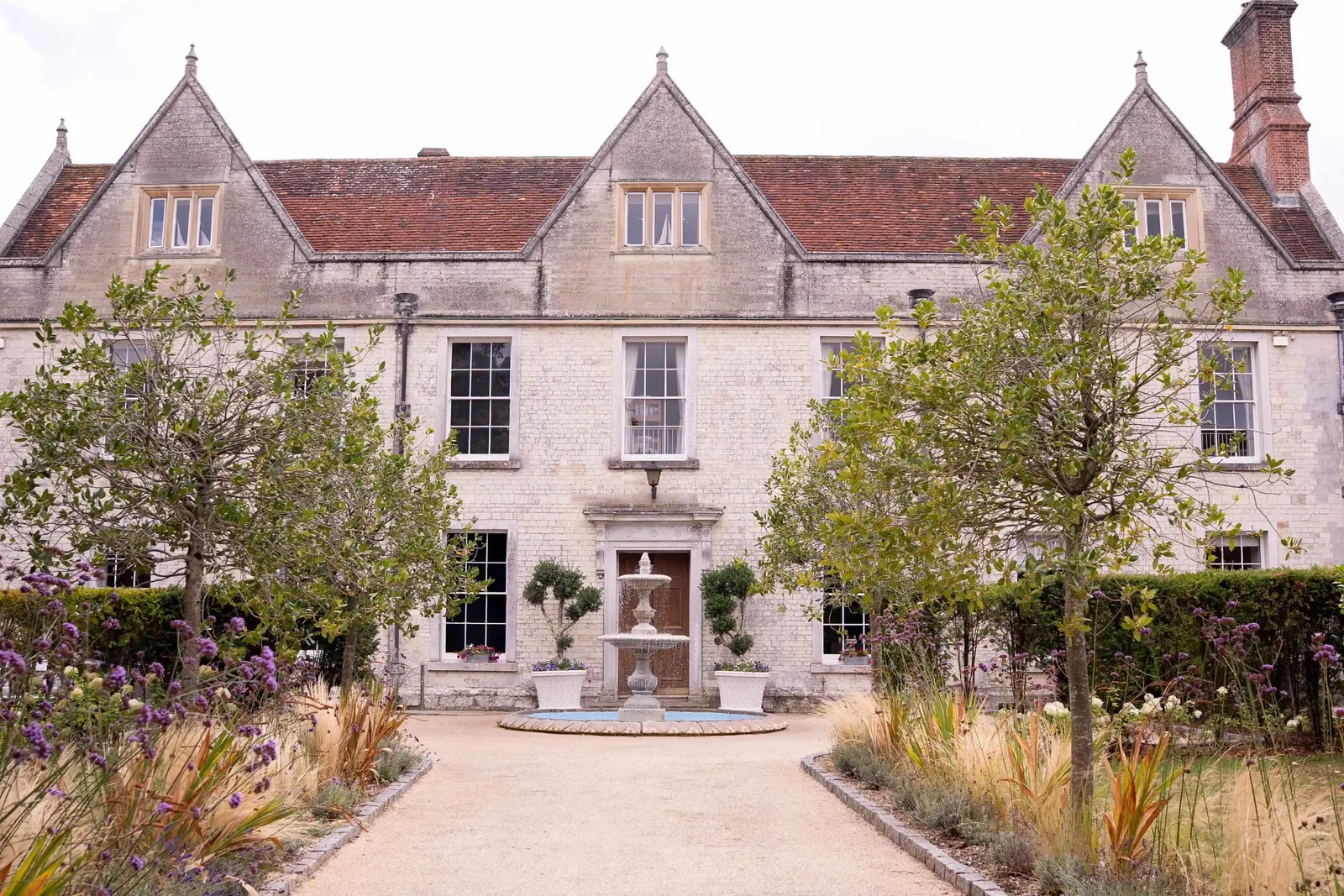 The stone front of Froyle Park with clipped bays either side of the door