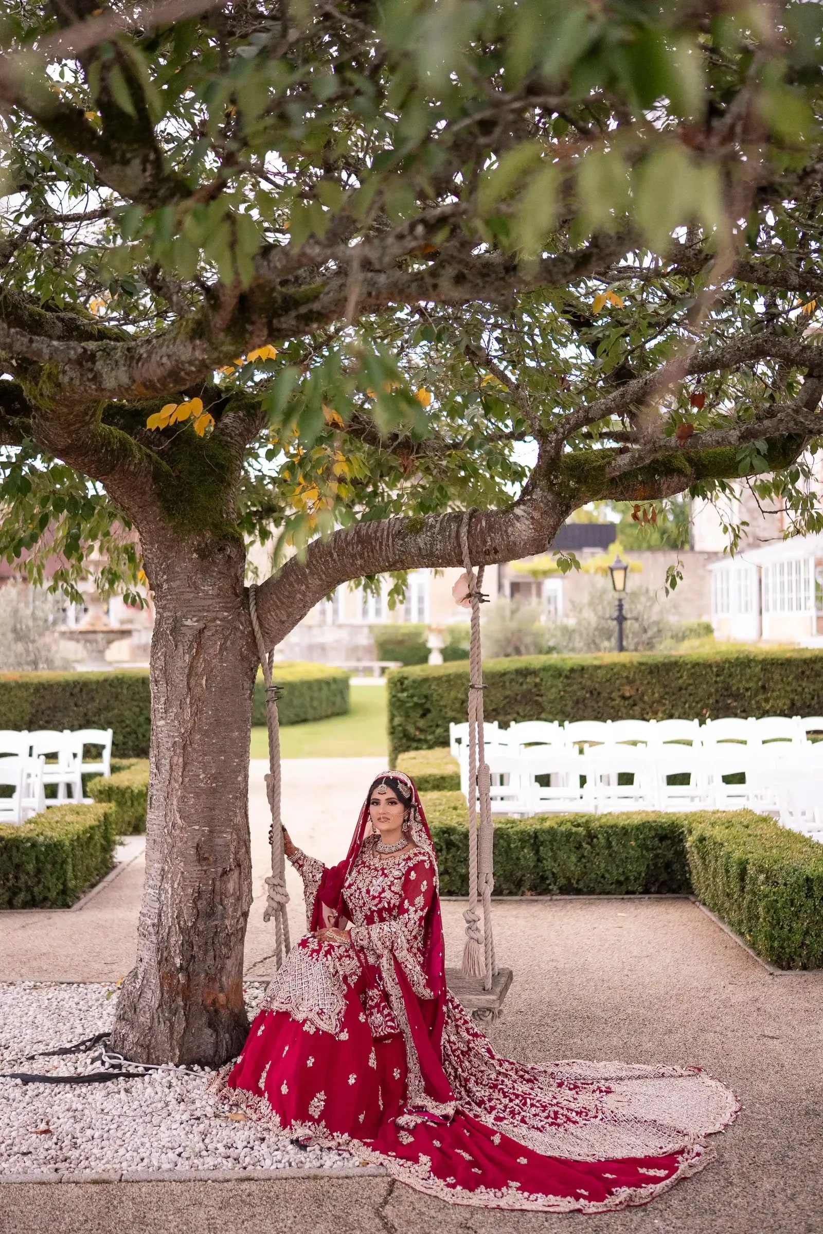 Bride seated on a rope swing under the tree, the ceremony chairs set out behind her