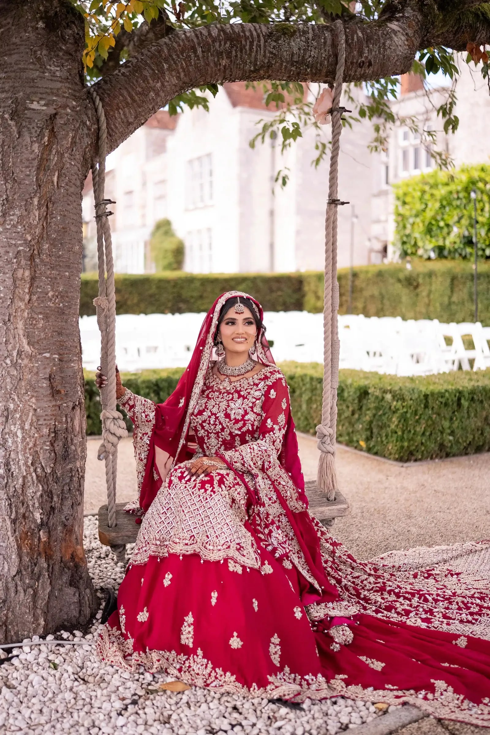 Bride holding the ropes of the swing, her lehenga spread over the white stones