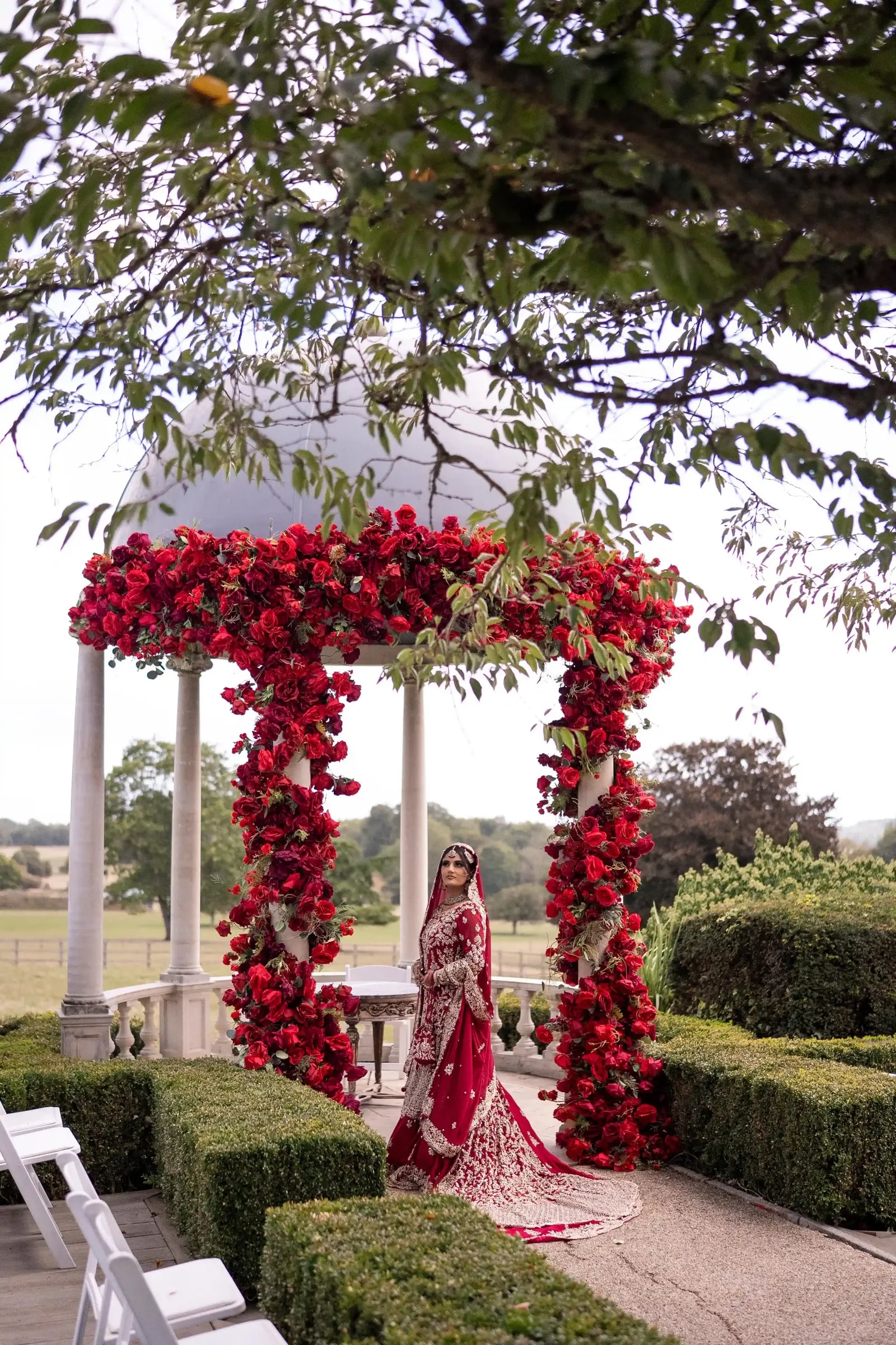 Bride framed by the red rose arch, her train falling down the step