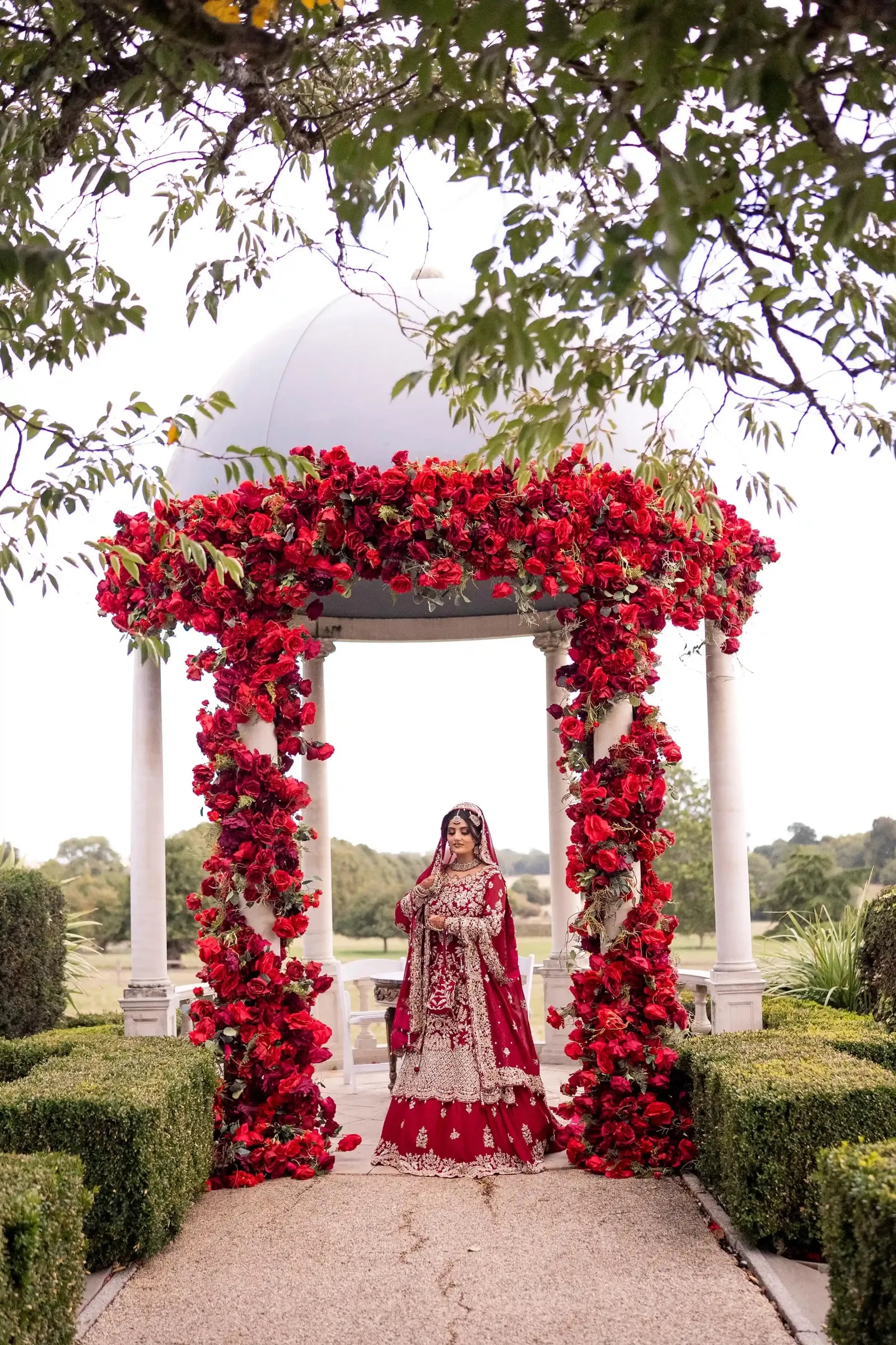 The rose-covered arch seen through the branches, the bride standing beneath it