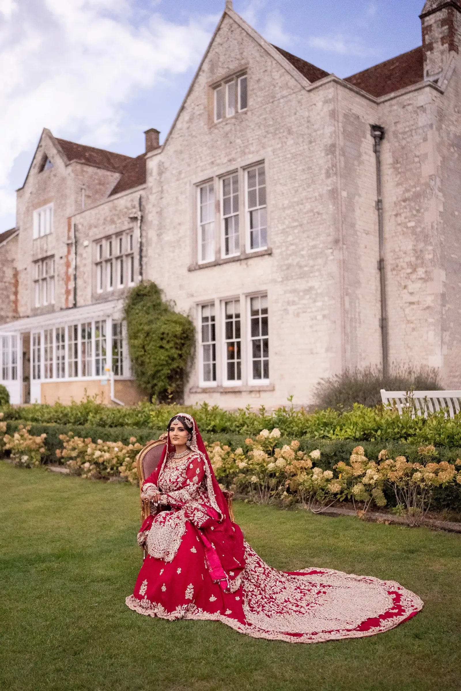 Bride on the lawn beside the rose border, the stone house rising behind her