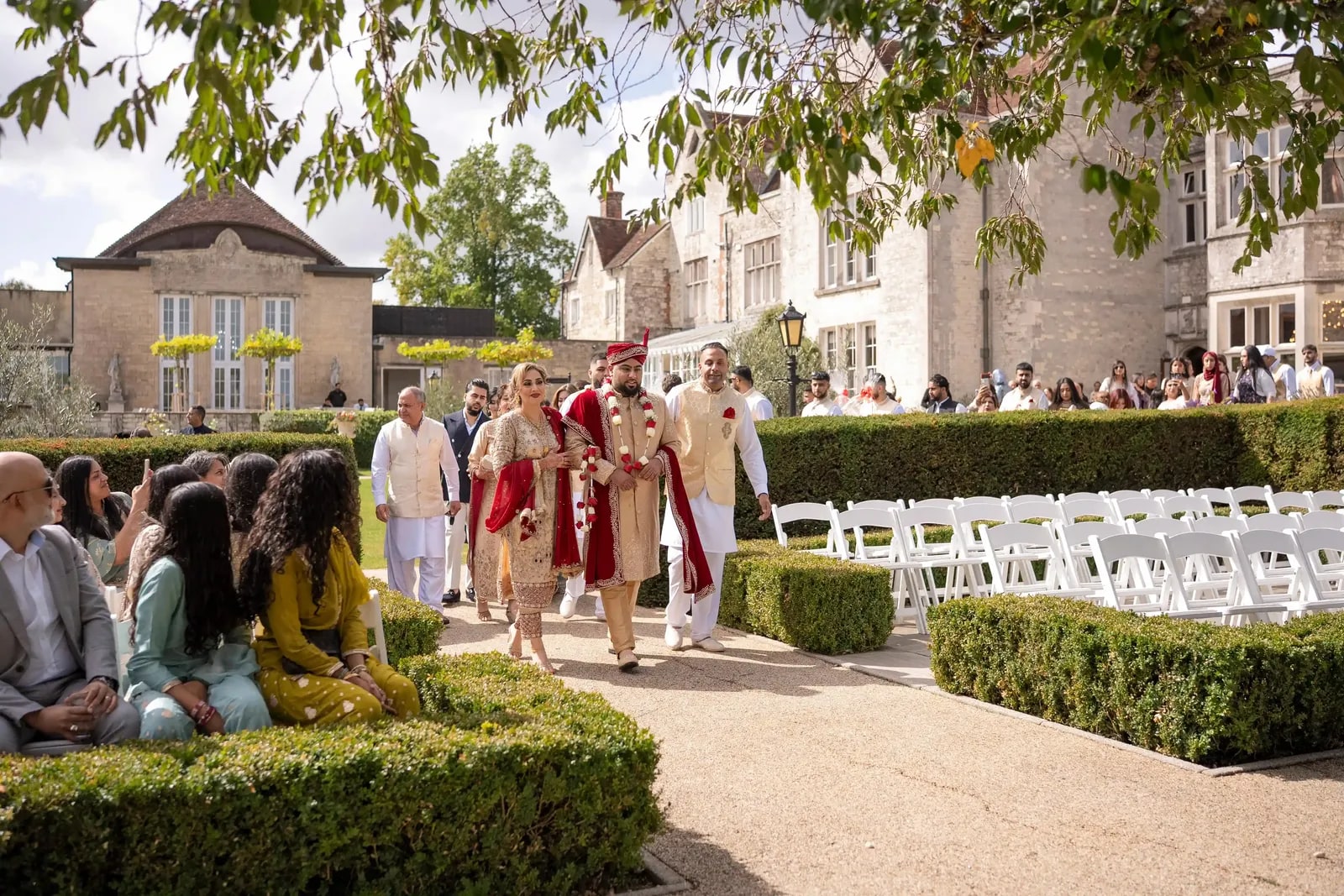 Groom in red and ivory walking in past seated guests to the ceremony
