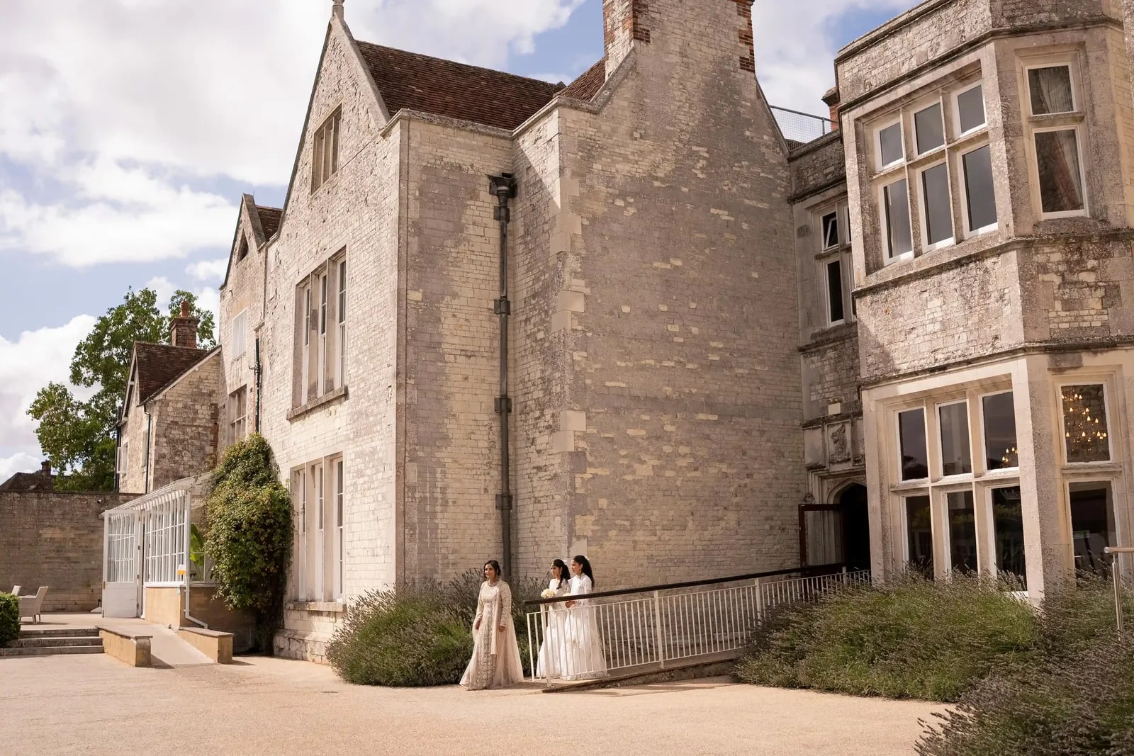 Two women waiting at the foot of the stone house, small against its full height