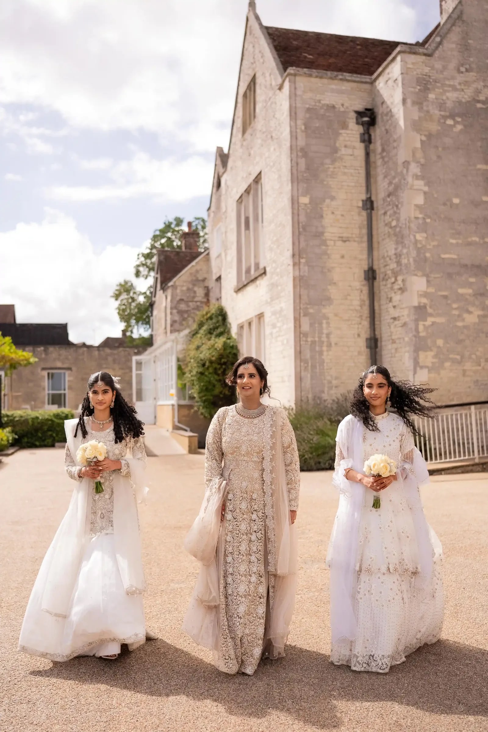 Three women in ivory walking together along the path with bouquets