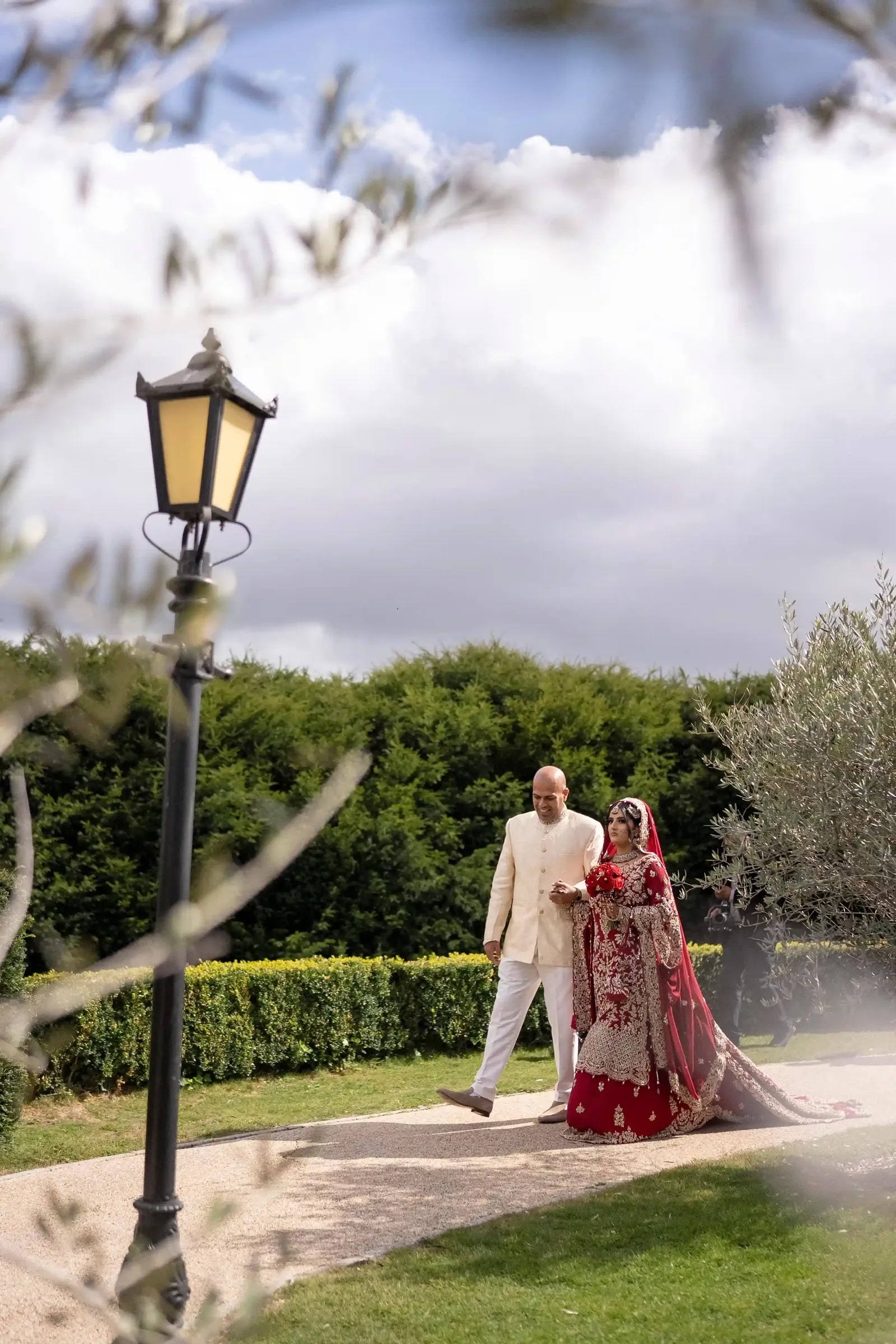 Bride and her father on the path past the lamp post, framed by olive branches