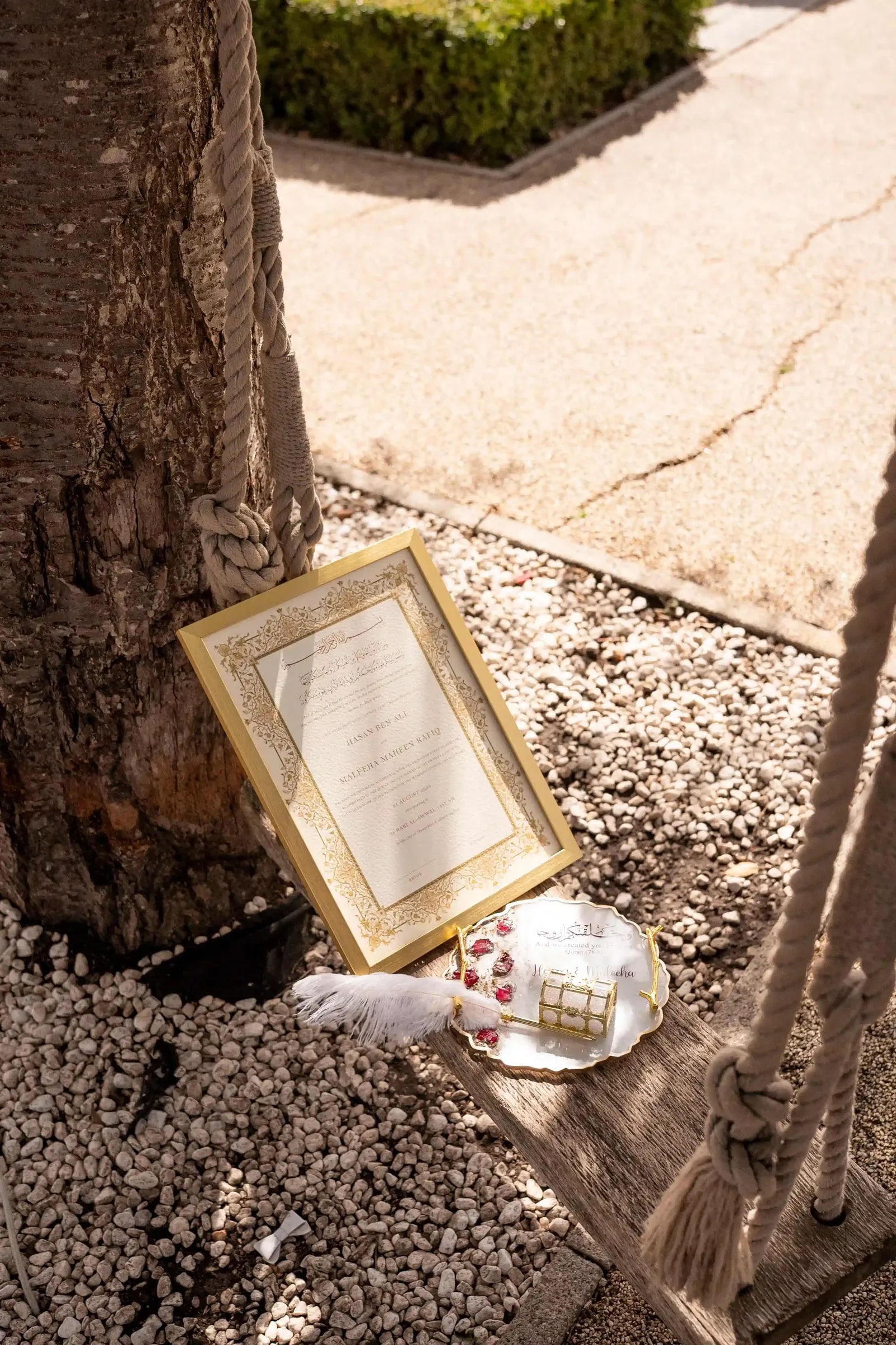 The framed nikkah certificate propped against a tree with a feather pen beside it
