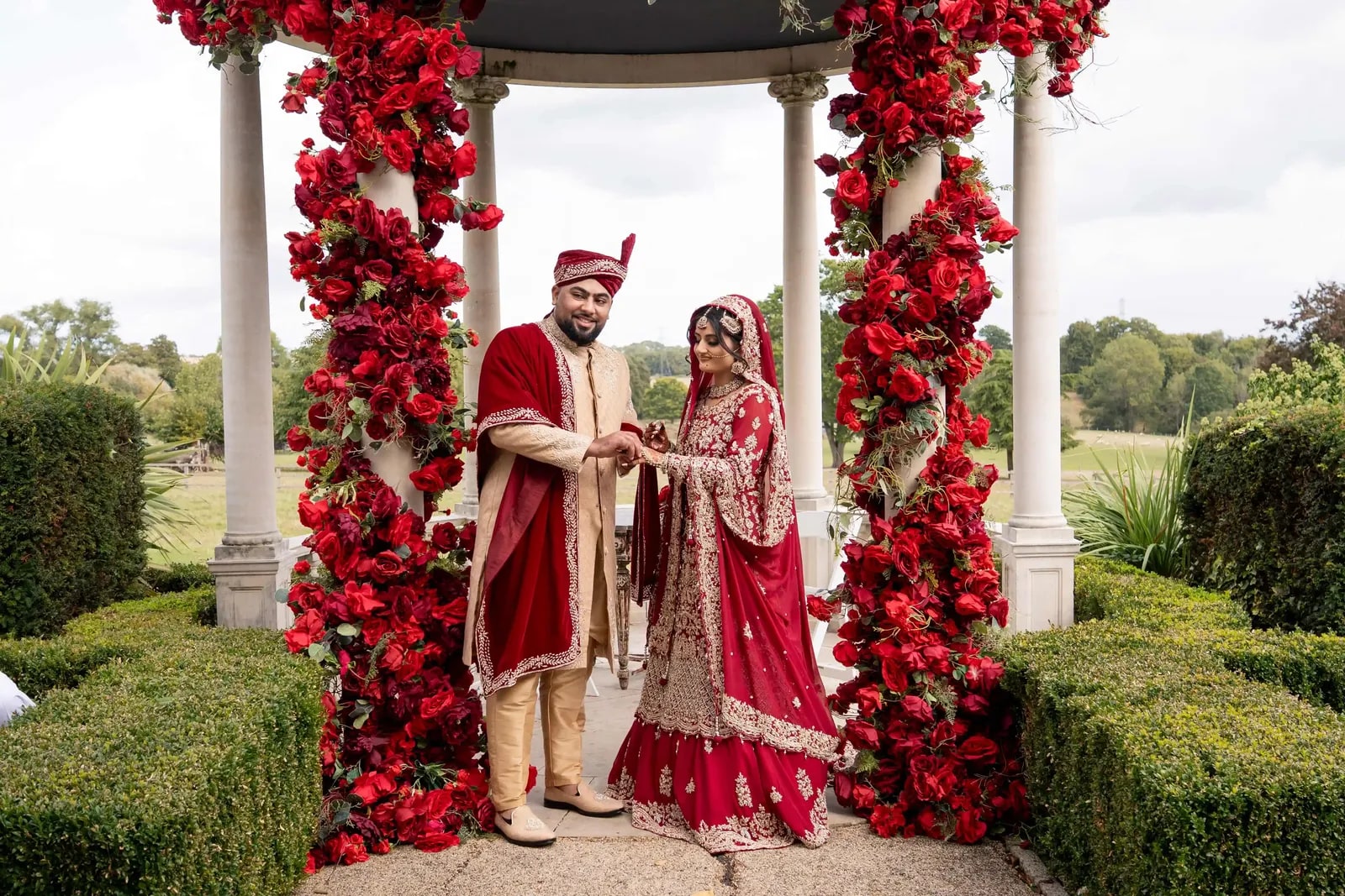 Groom holding both his bride's hands beneath the rose-covered arch
