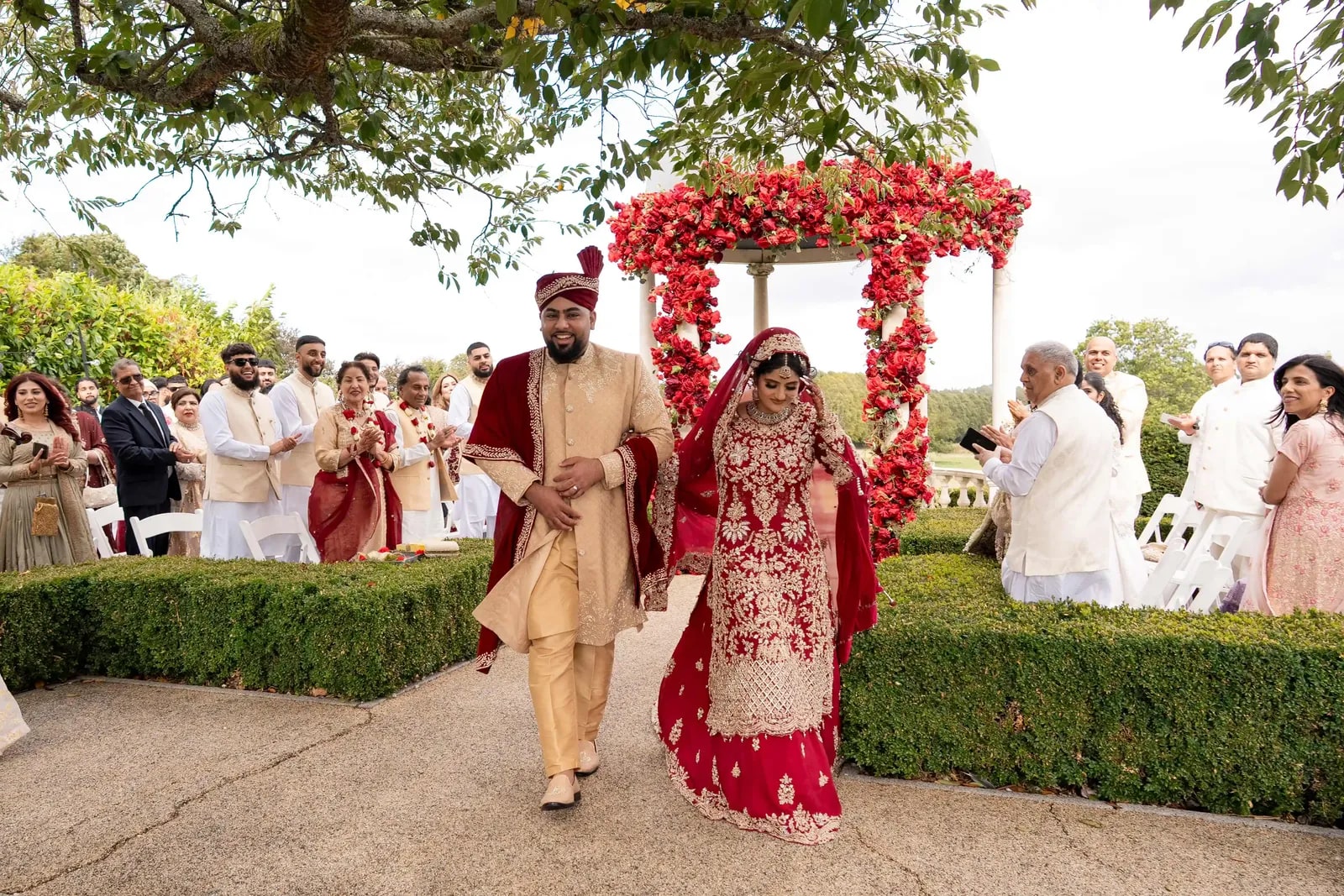 Groom leading his bride along the clipped hedge path, guests watching behind