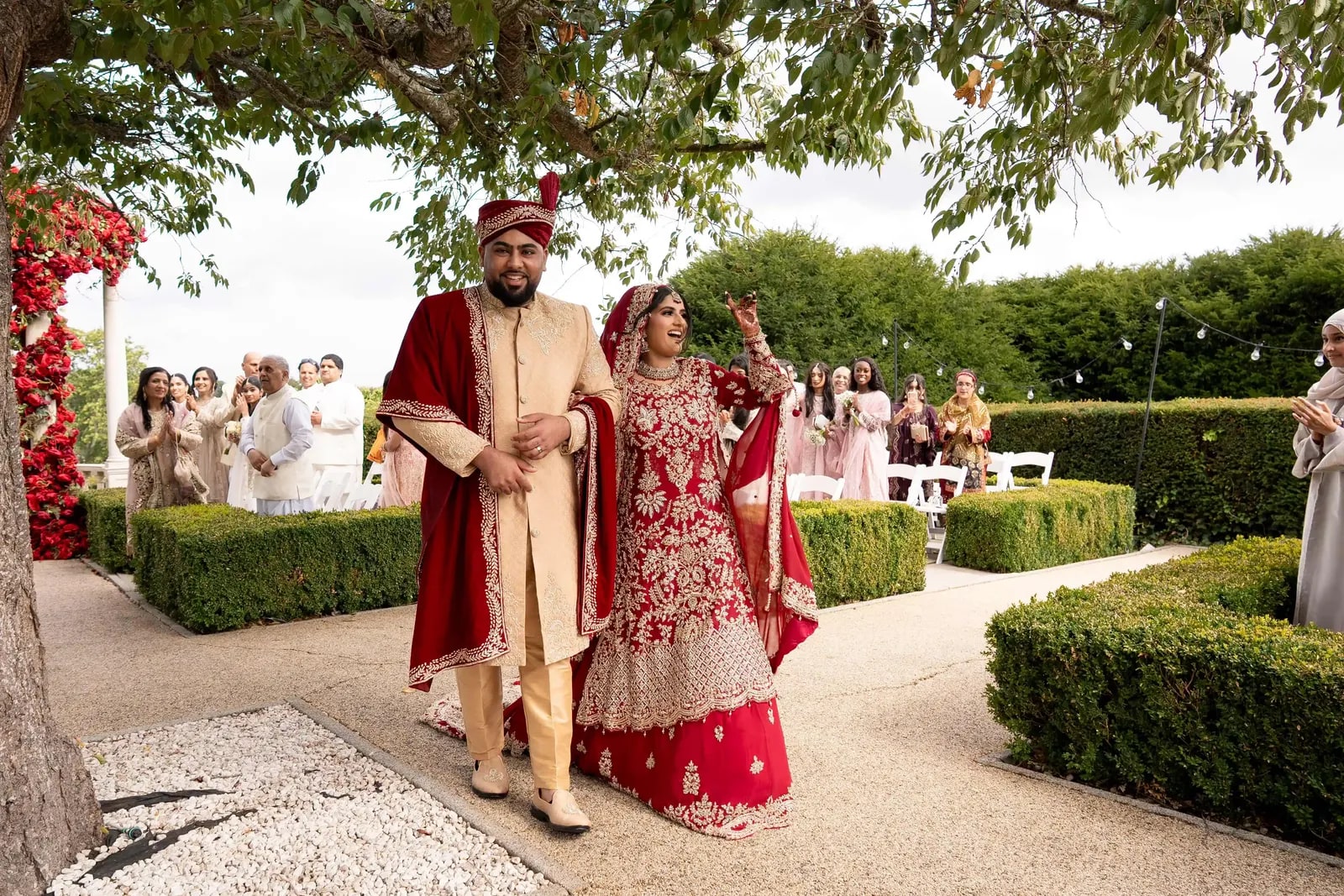 Bride raising her hand as she and her groom walk back through the garden