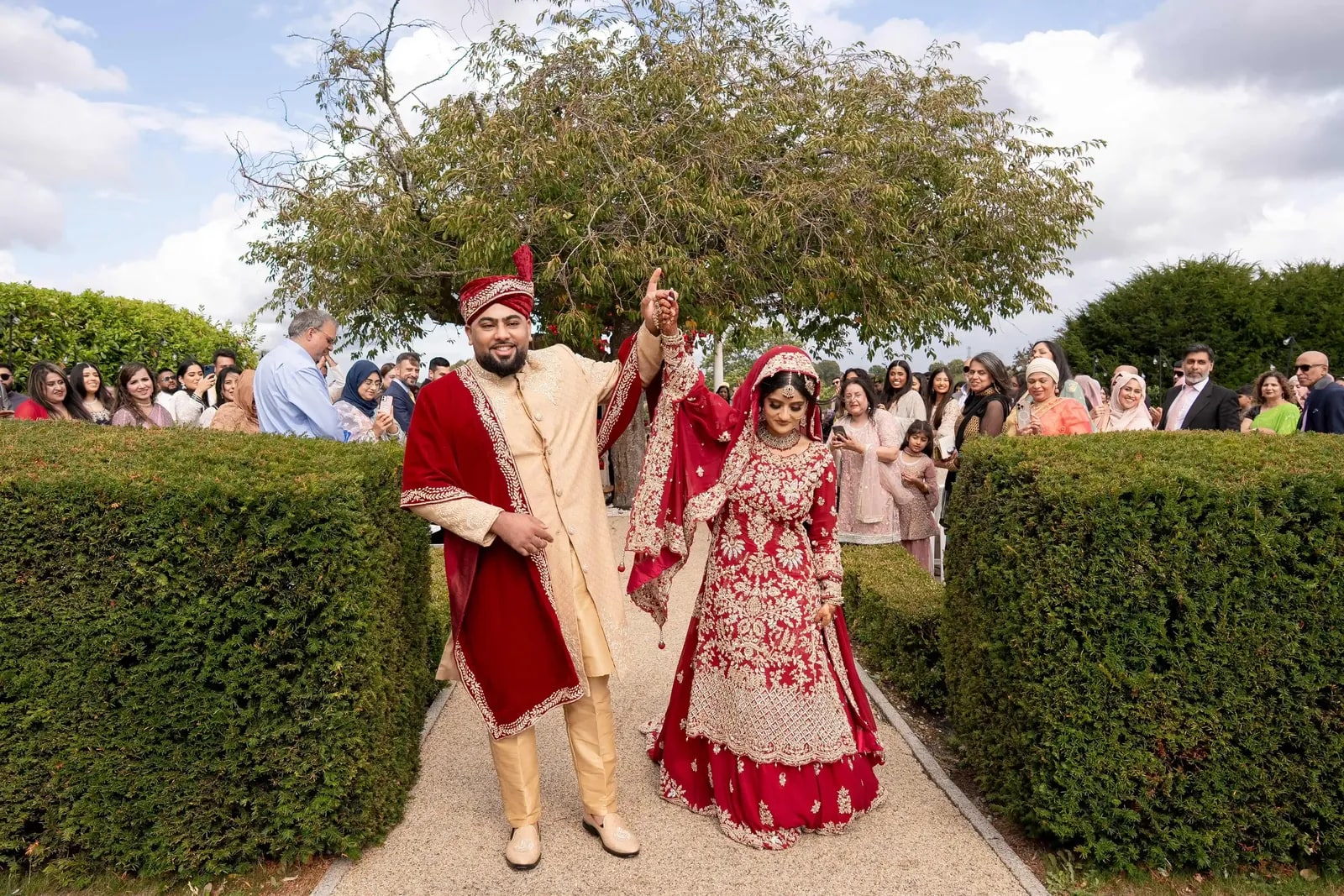 Couple walking the hedge path with their hands raised, guests lining the far side