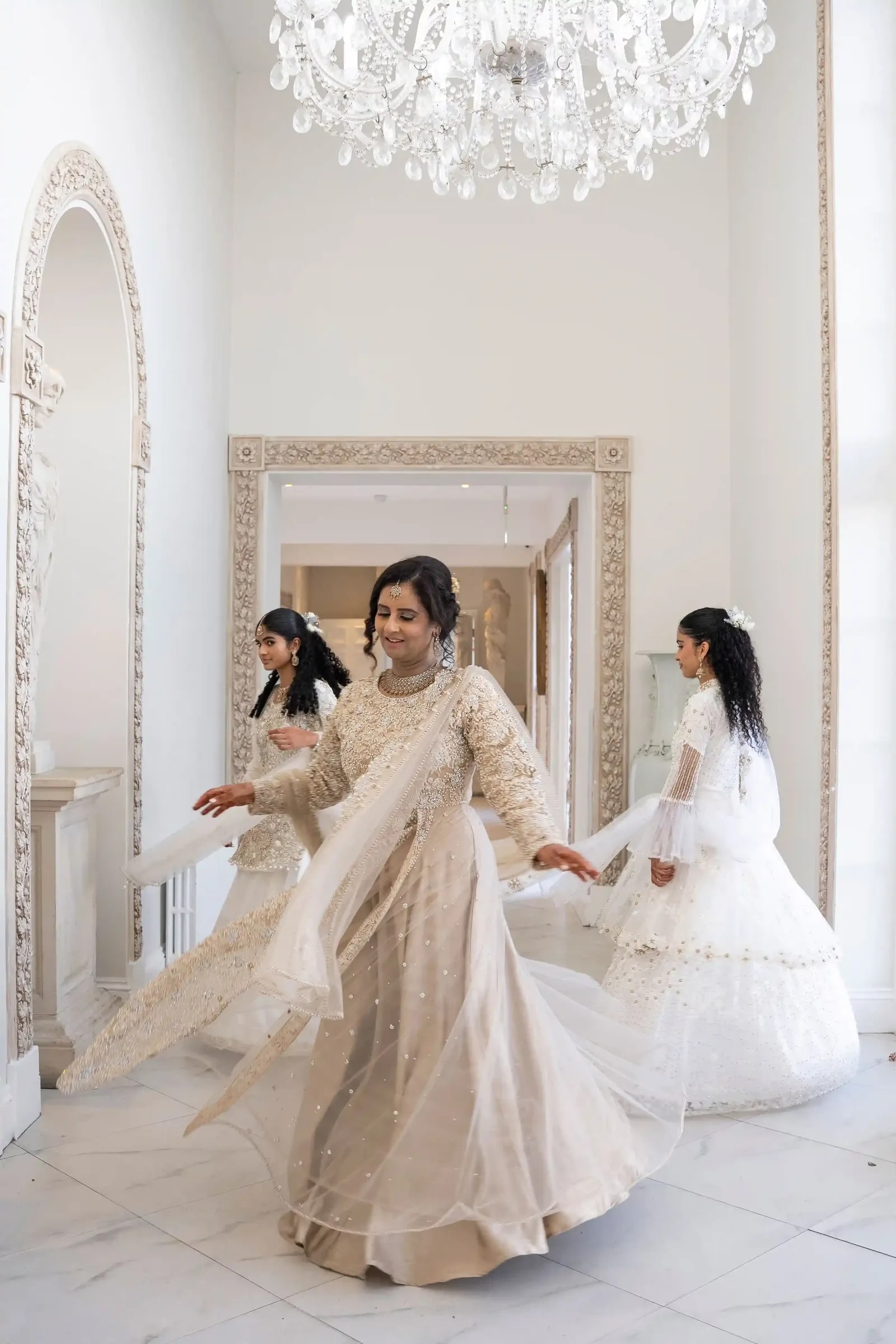 Woman in ivory turning mid step in a marble hallway beneath a chandelier