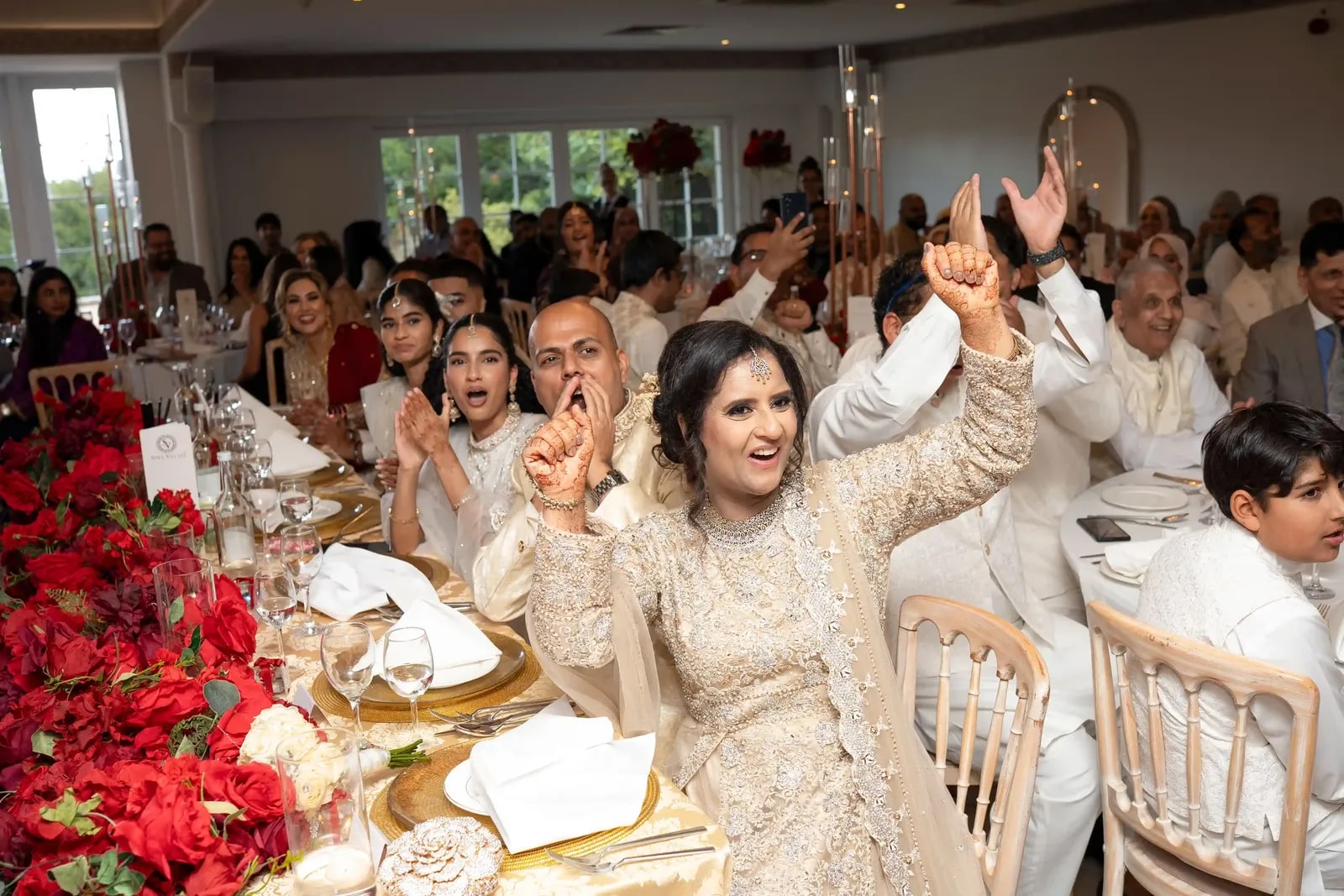 Guests at the long table cheering, red roses running down the centre