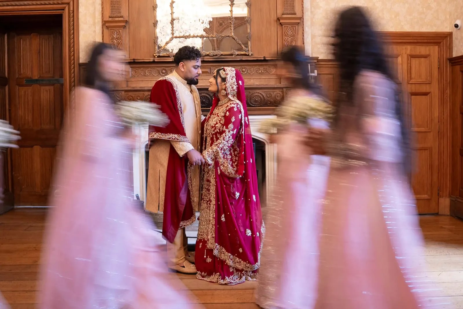 Bride and groom still in the doorway as her party in pink rushes past, blurred