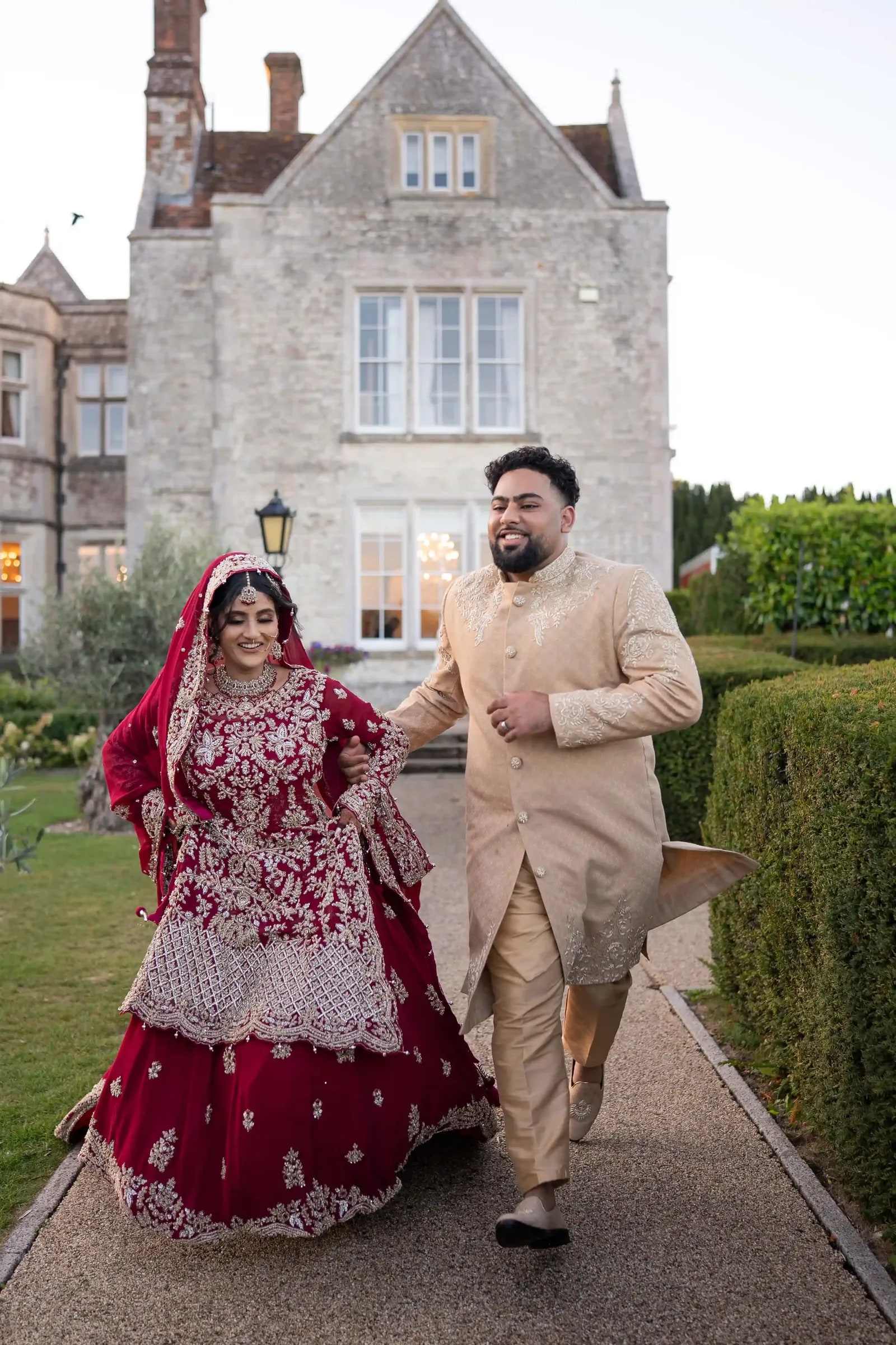 Bride laughing as her groom hurries her along the path, her lehenga swinging