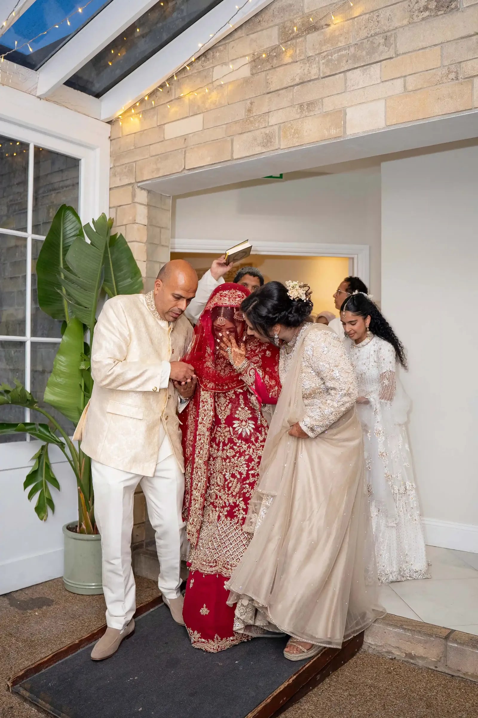 The bride's family holding a Quran over her head as she is walked out through the doorway