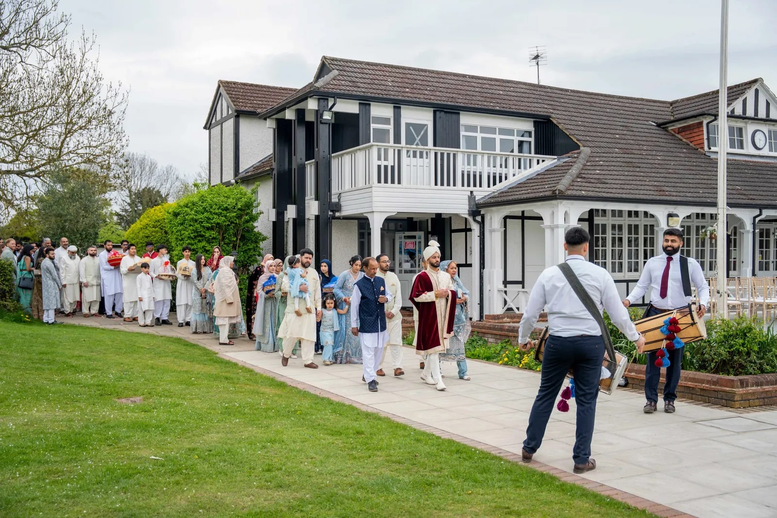 Guests queuing along the path outside the Tudor-fronted pavilion, a dhol player alongside