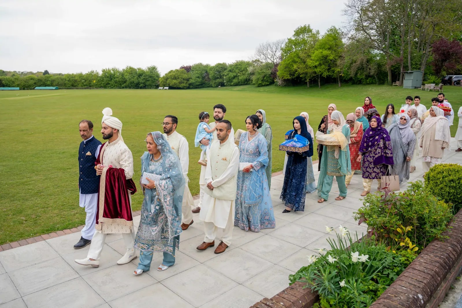 Guests in pale blue walking the path beside the cricket ground