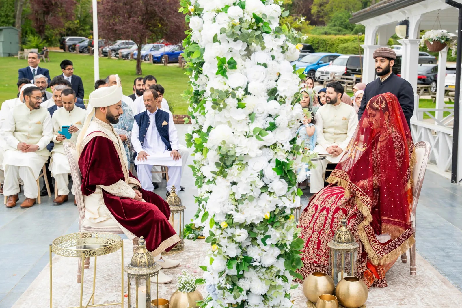 Bride and groom seated either side of a white flower column during the nikkah
