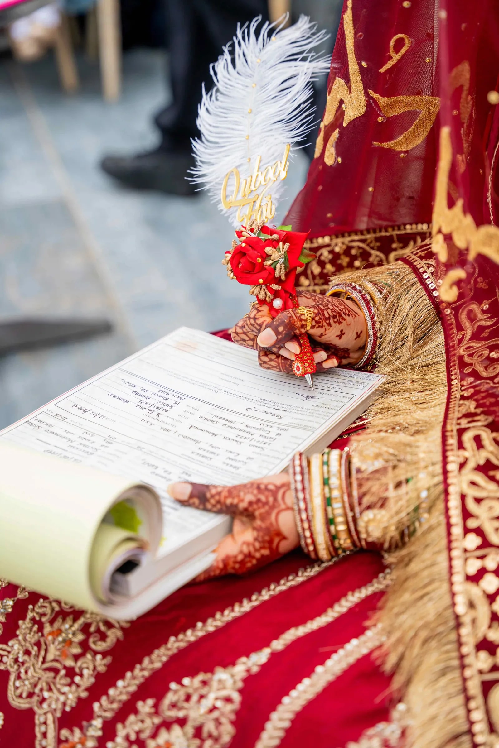 The bride's hennaed hand turning the page of the nikkah nama on her lap