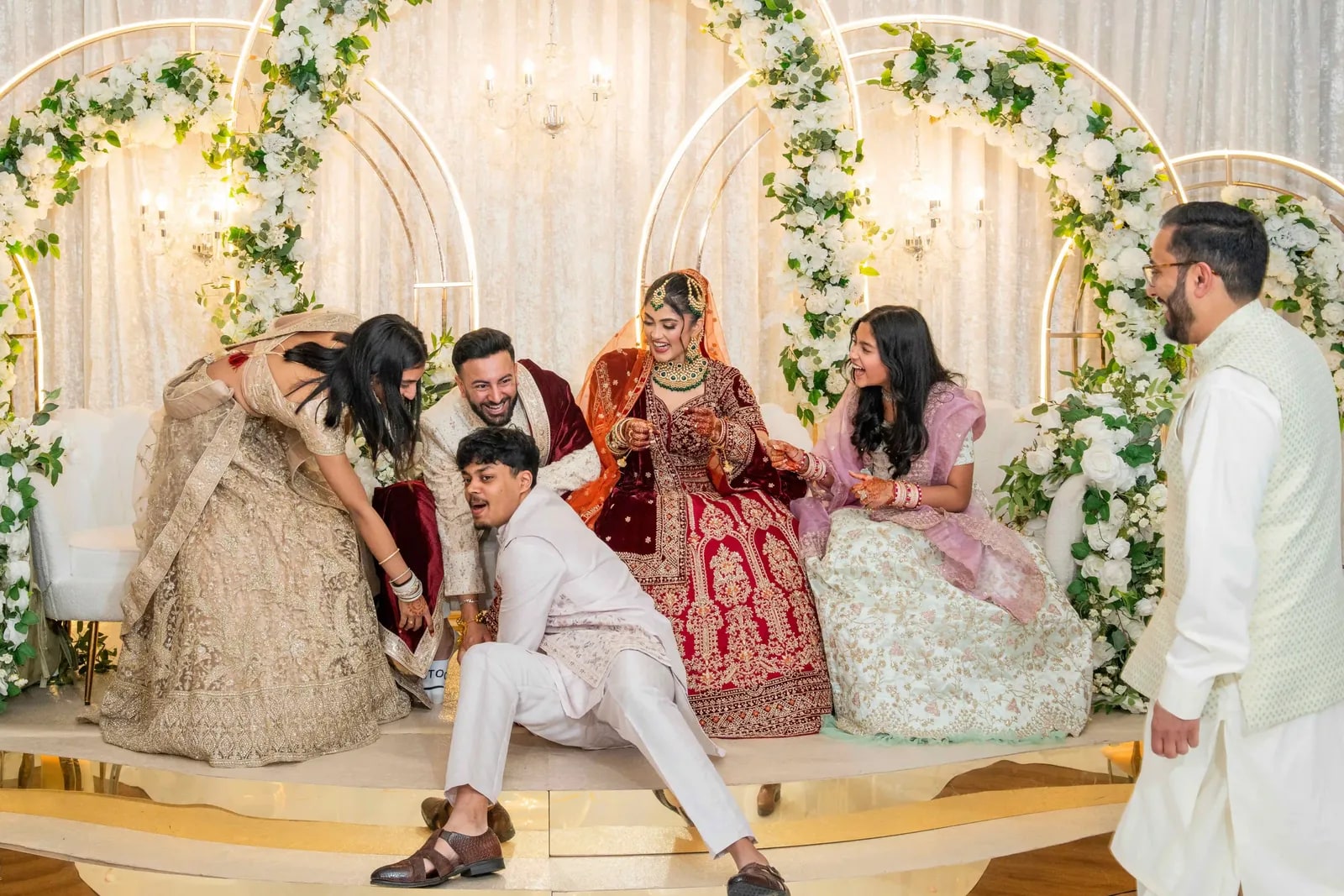 The couple on the stage as young men crouch to hide the groom's shoes