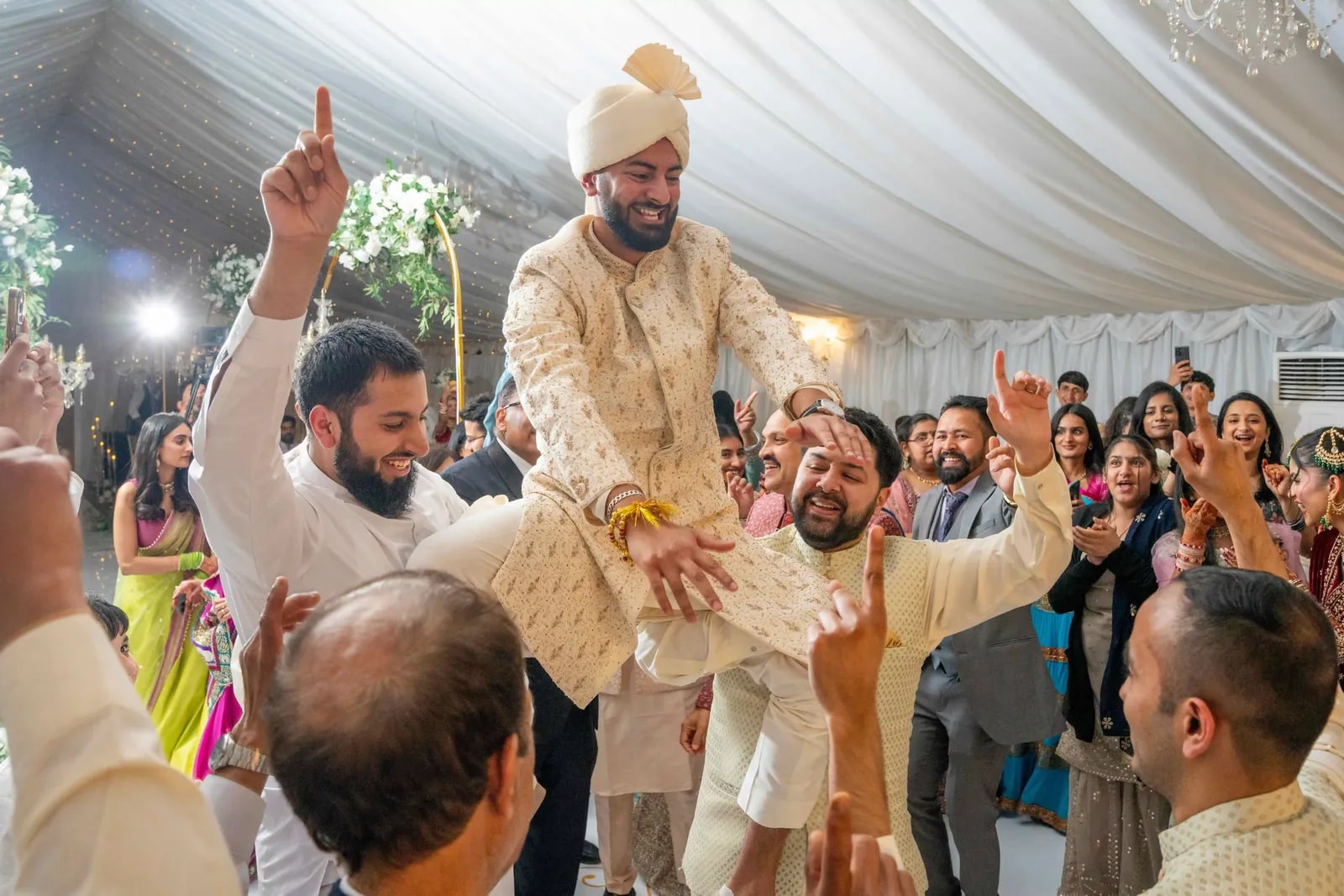 Groom carried in on shoulders through the crowded marquee, his hand raised