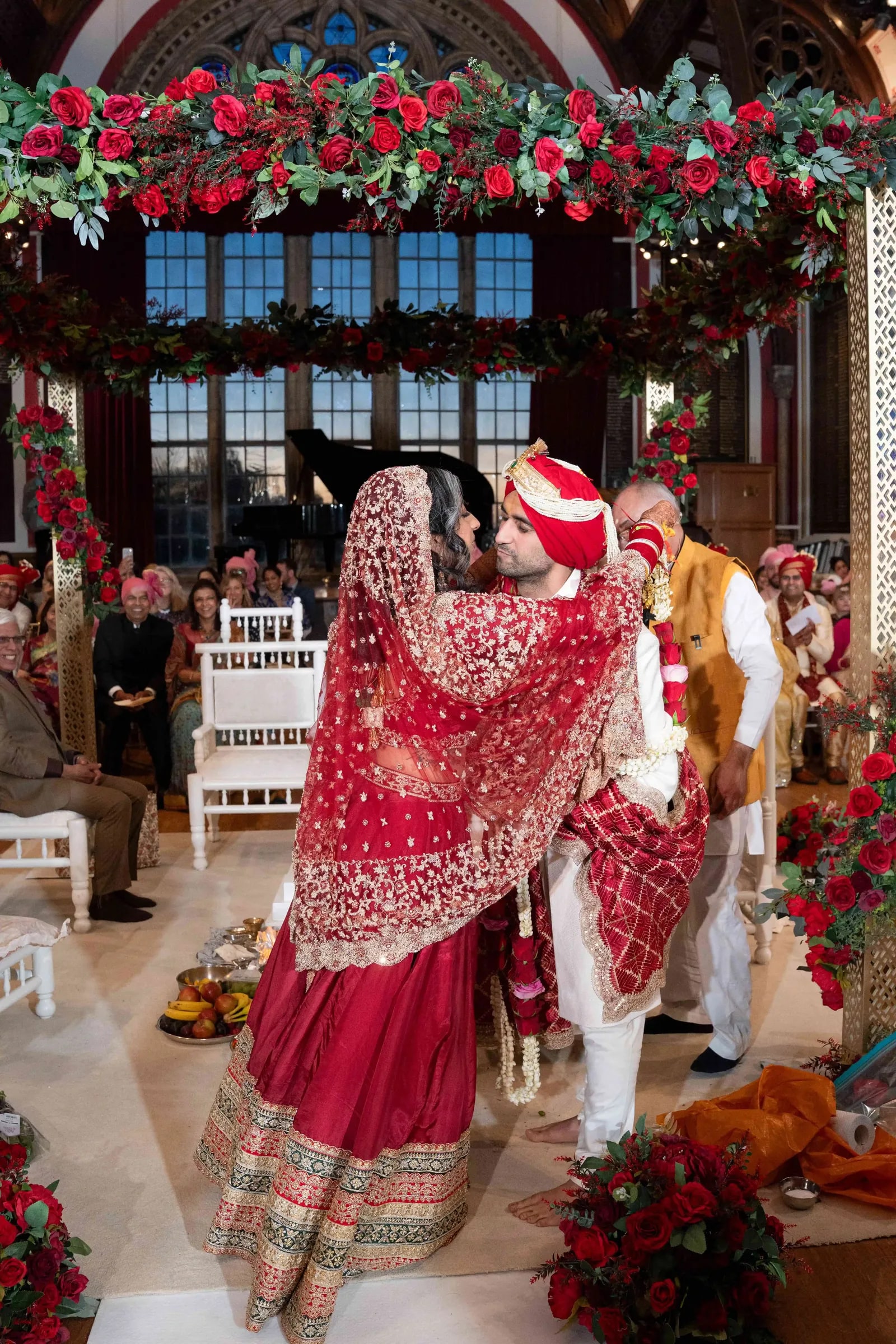 Bride and groom exchanging garlands beneath the red rose mandap