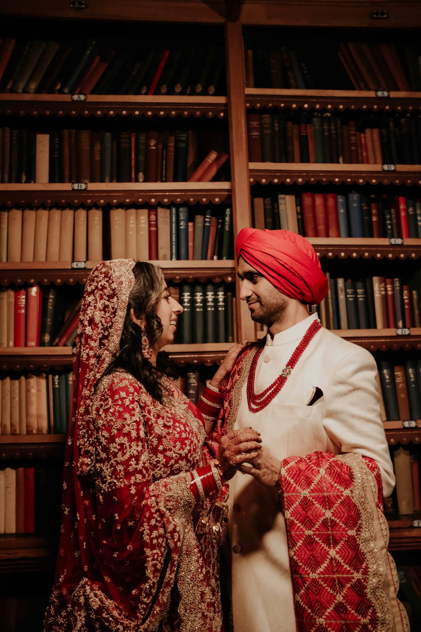 Bride and groom face to face before the bookshelves, he in a red turban