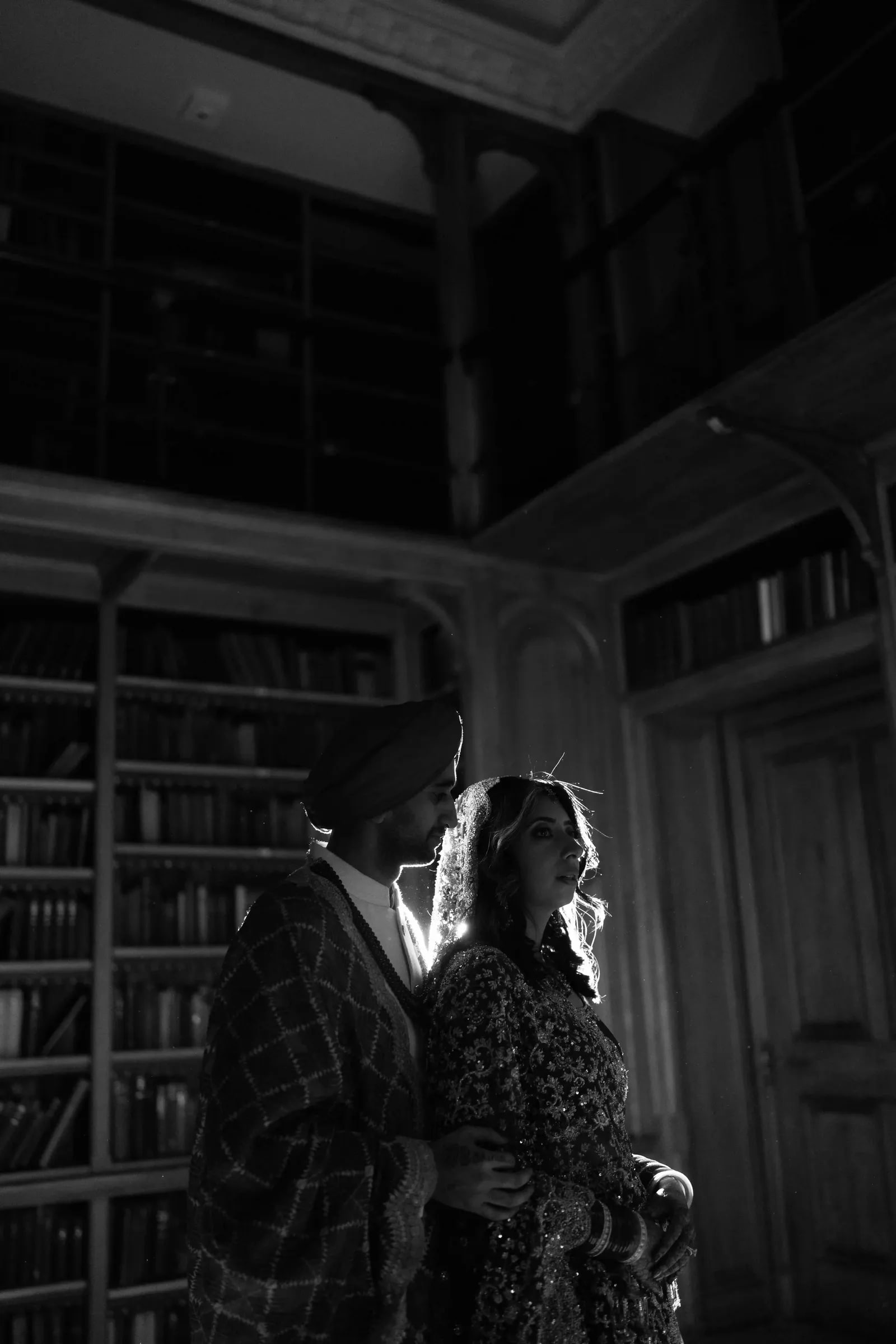 Couple rim lit in the dark library, close together, in black and white
