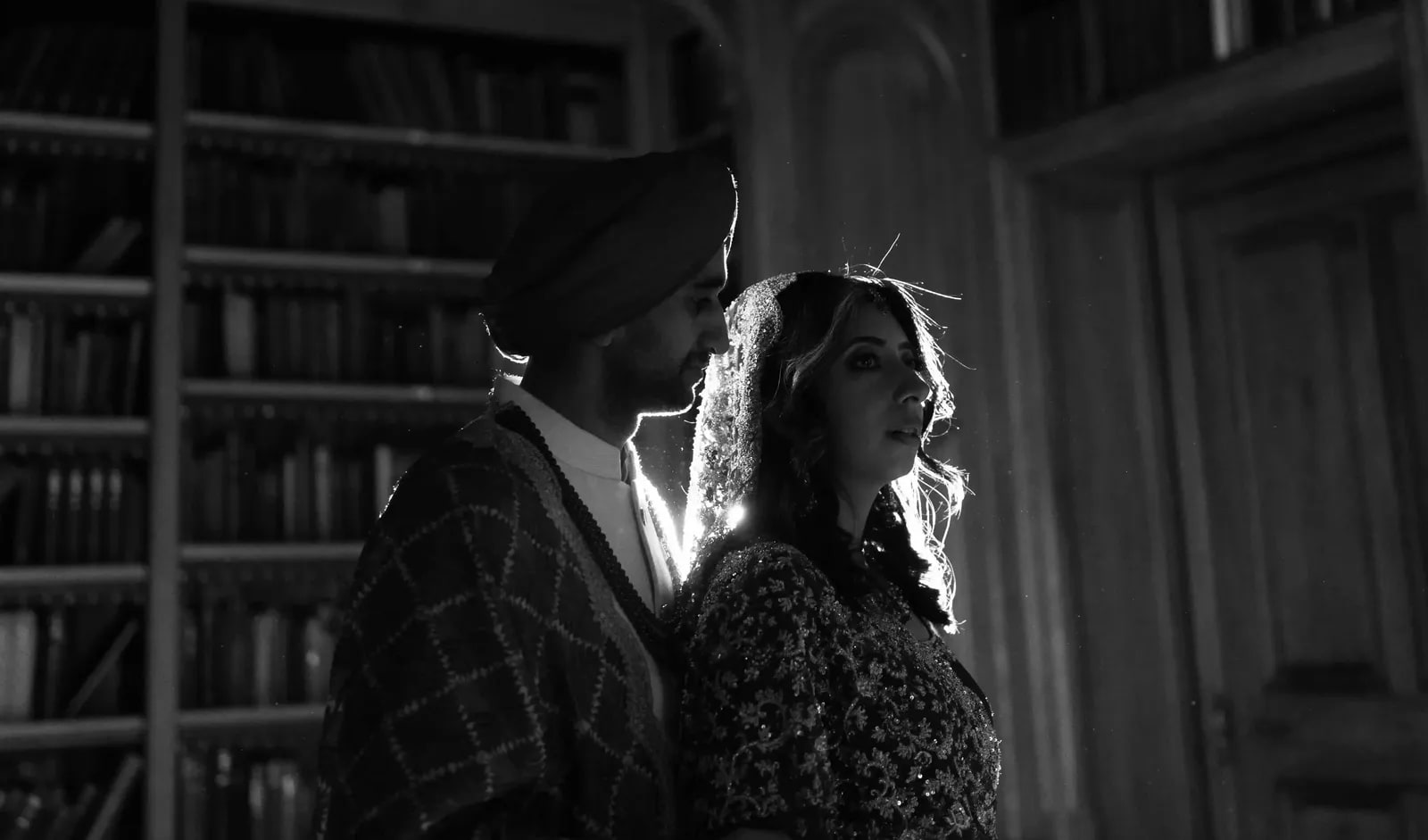 Couple rim lit in the dark library, close together, in black and white