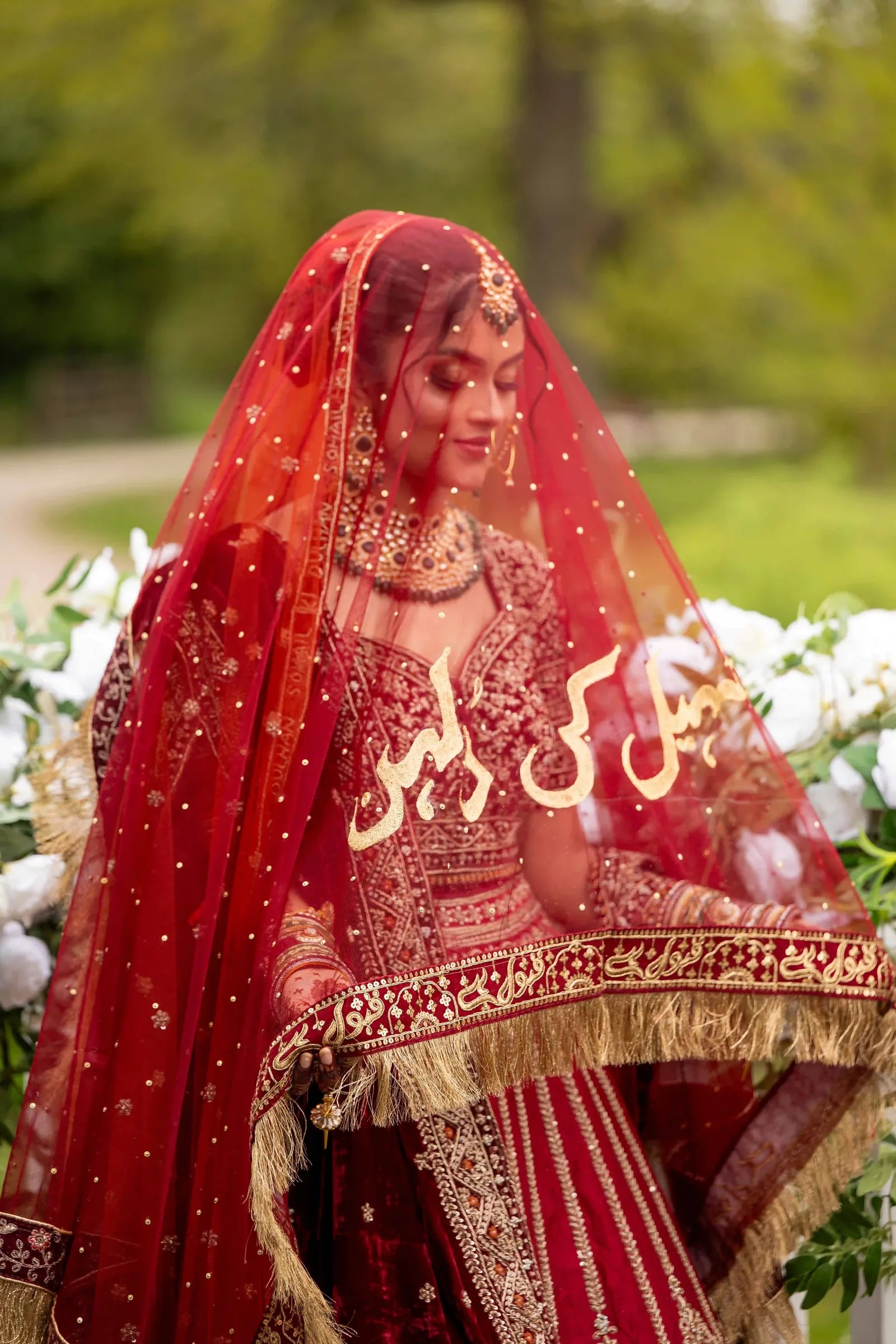 Bride beneath a red dupatta embroidered in gold with the couple's names in Urdu