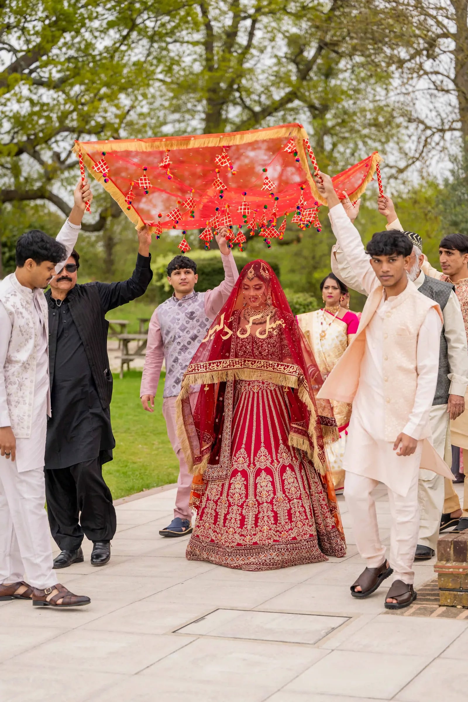Bride walked in under a red and orange cloth held over her by her brothers
